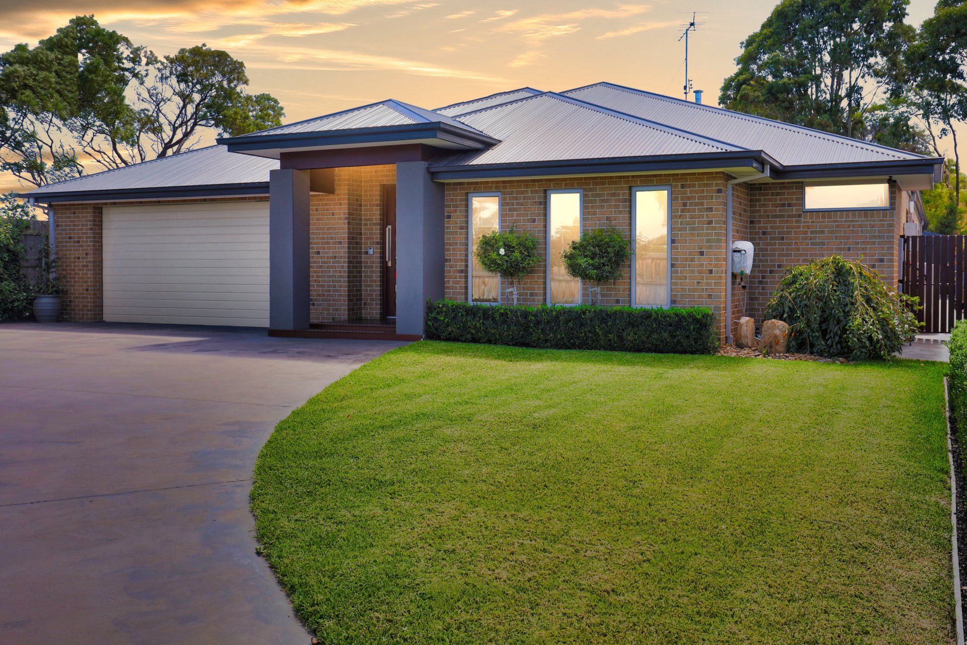 Single-story brick house with a garage, front lawn, and curved driveway at sunset