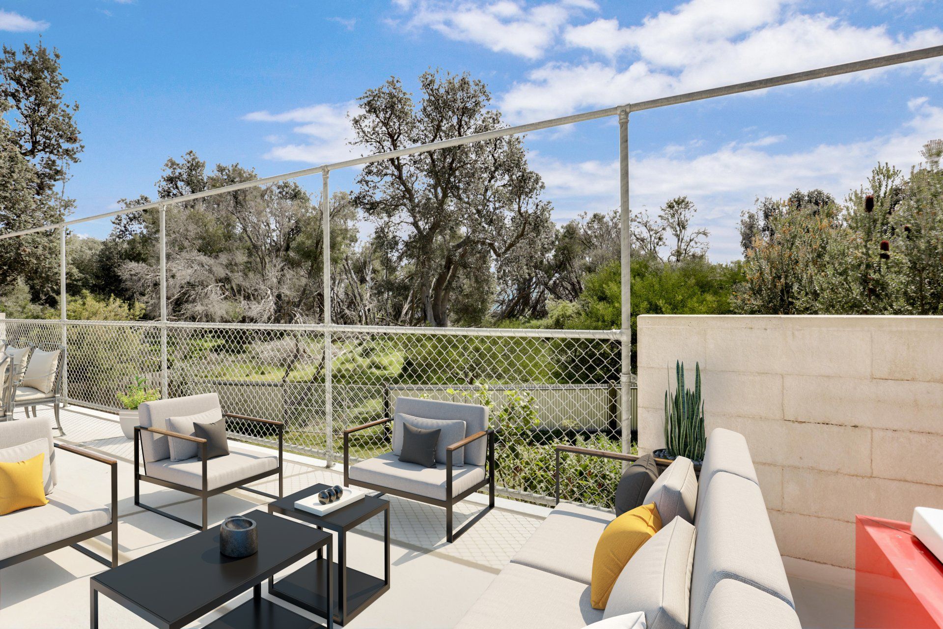 Outdoor patio seating with gray chairs, black table, and yellow pillows beside a fence and greenery