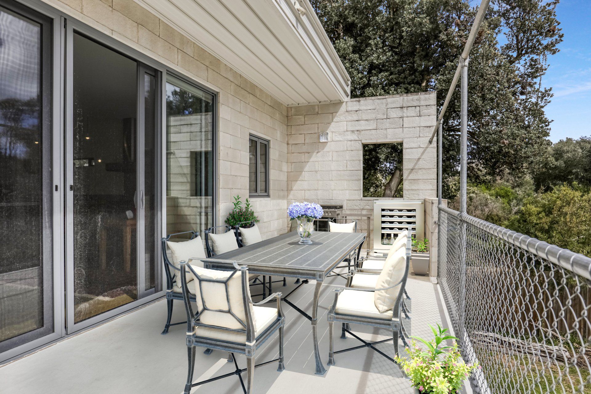 Patio dining area with glass table and chairs beside a sliding door and white brick wall