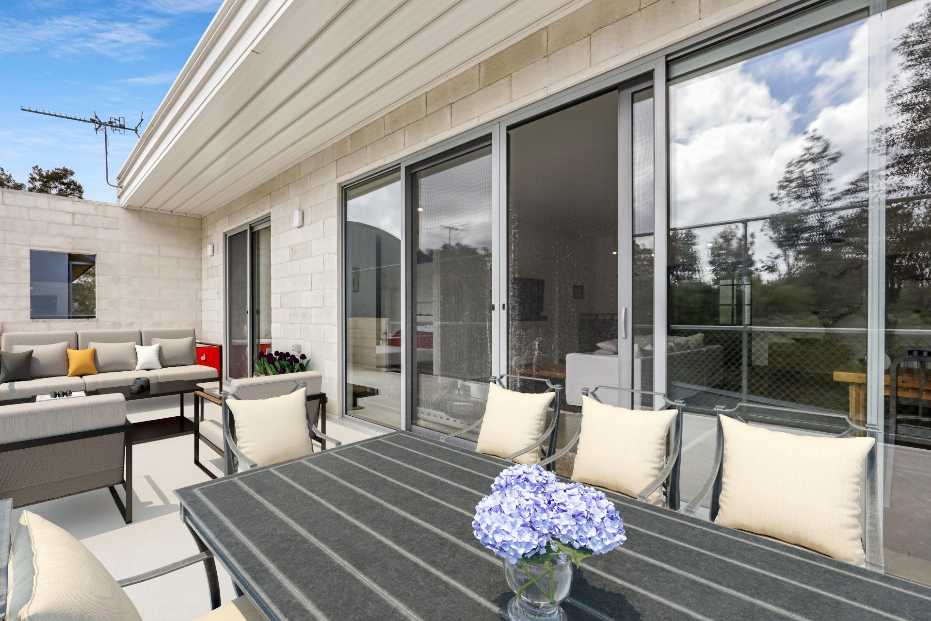 Modern patio with dining table, cushioned seating, and sliding glass doors under a covered overhang