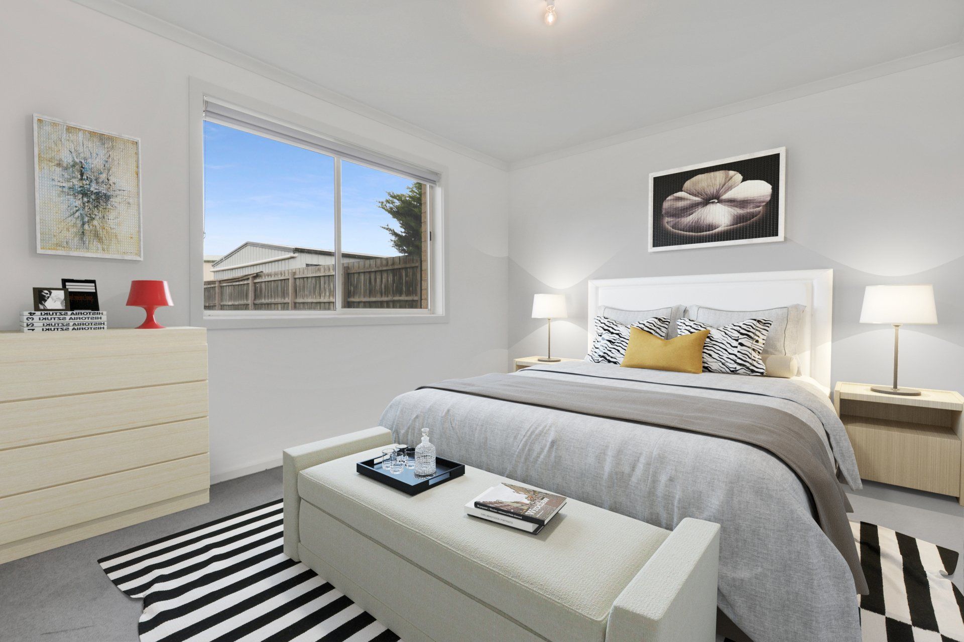 Bright modern bedroom with a bed, dresser, lamps, striped rug, and a large window