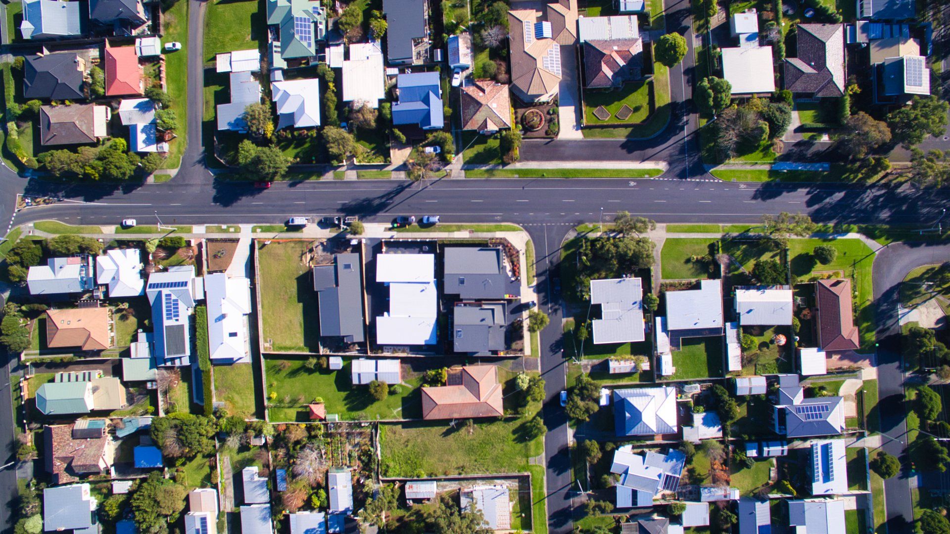Aerial view of a suburban neighborhood with houses, trees, and a road running horizontally through the center.