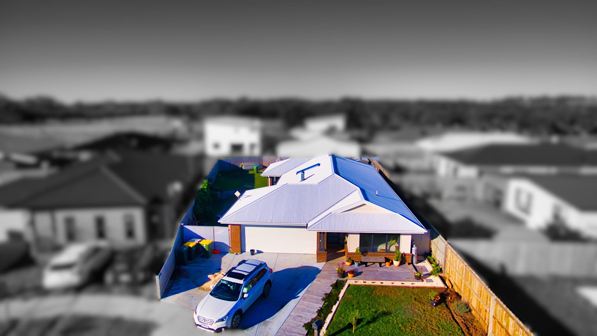 Aerial view of a house with a white canopy tent and a blue car in the driveway, against a blurred neighborhood.