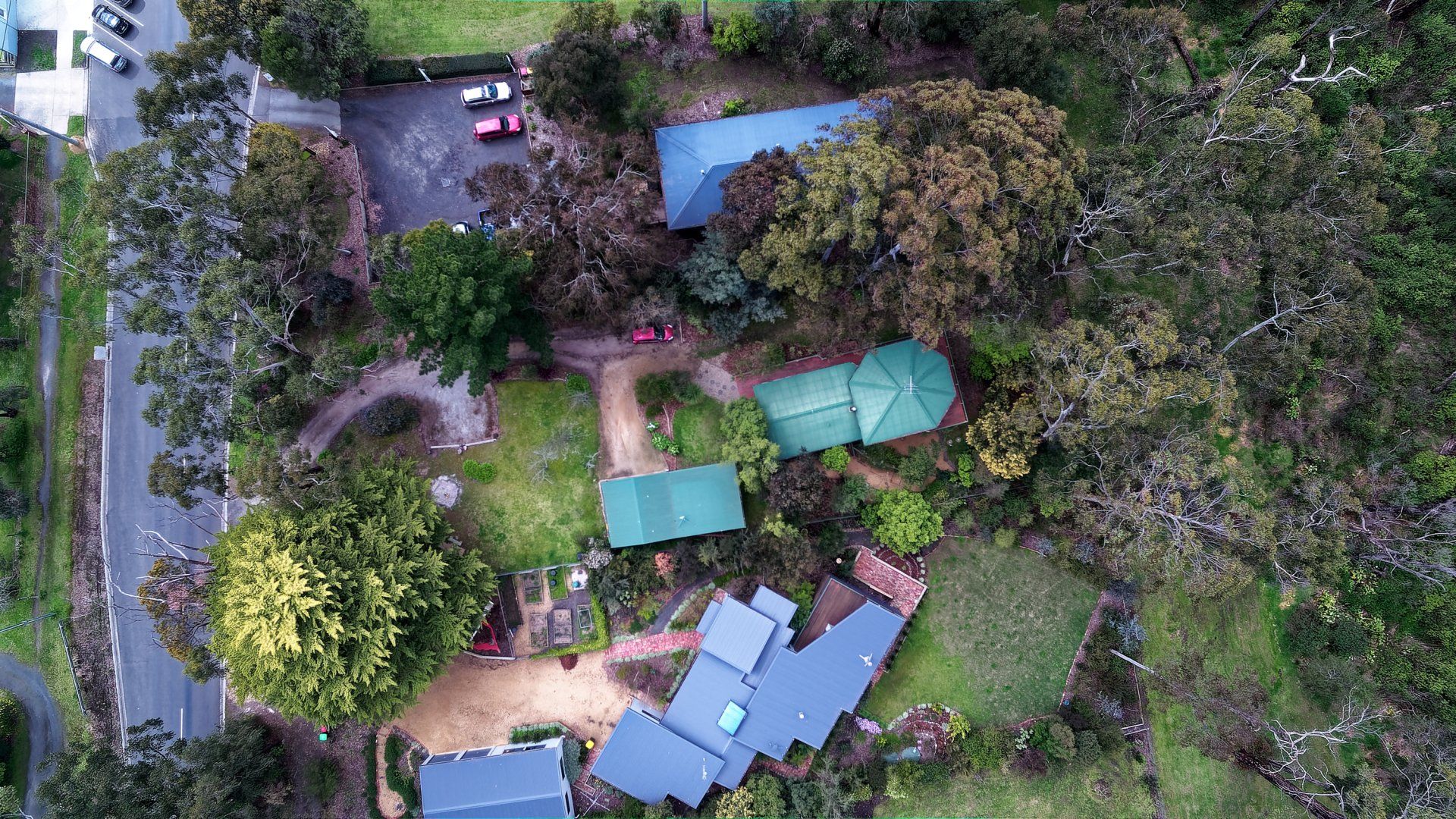 Aerial view of a small campsite with green tents and blue-roofed shelters beside dense trees and a road