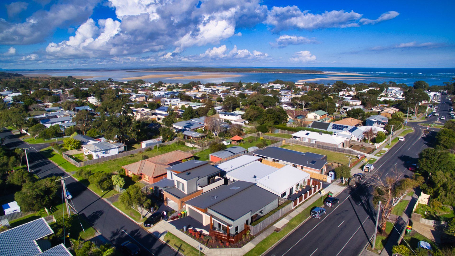 Aerial view of a coastal neighborhood with houses, roads, and blue ocean under a partly cloudy sky