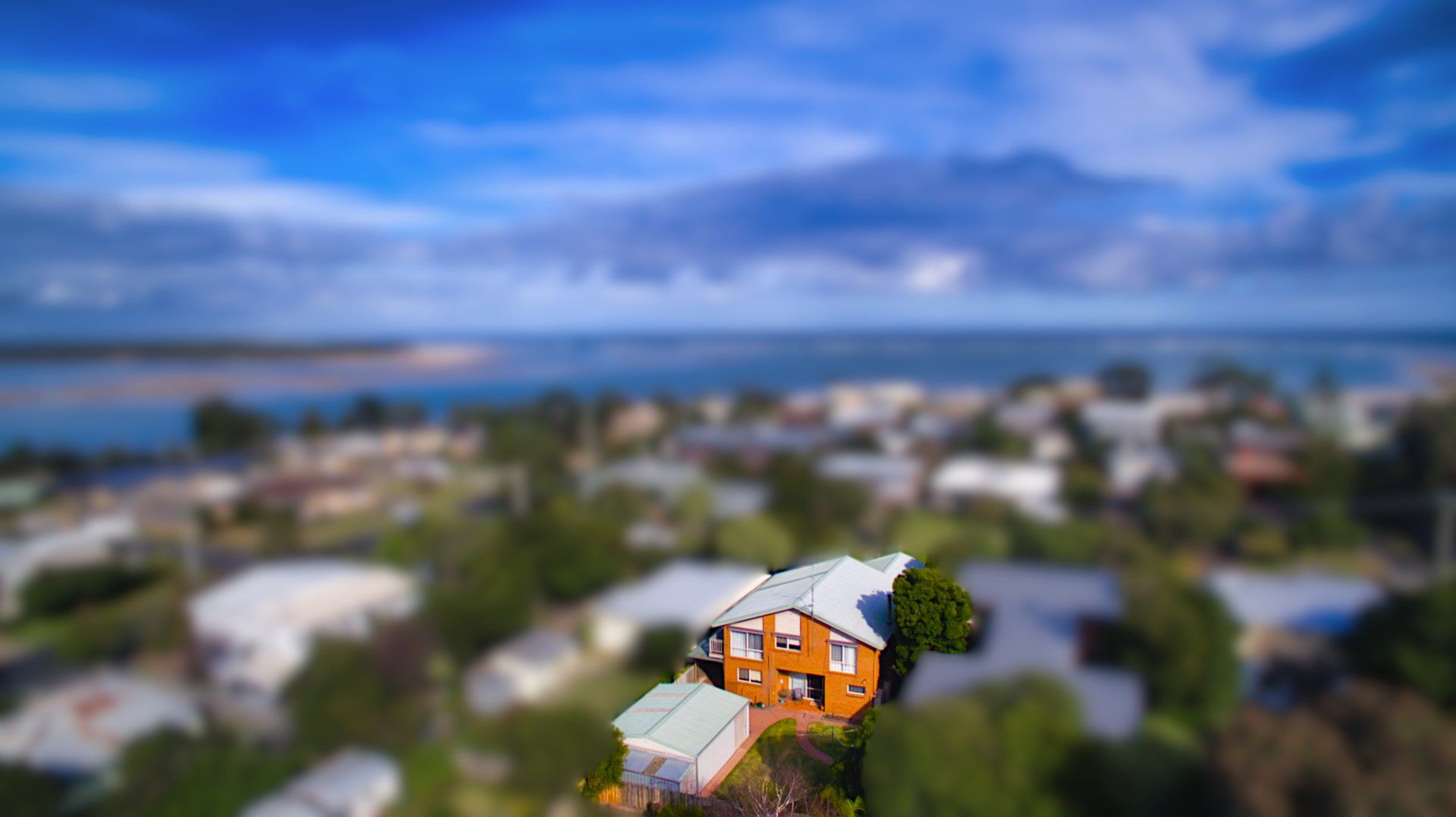 Aerial view of an orange house with a rooftop deck in a coastal neighborhood, with ocean and cloudy sky beyond.