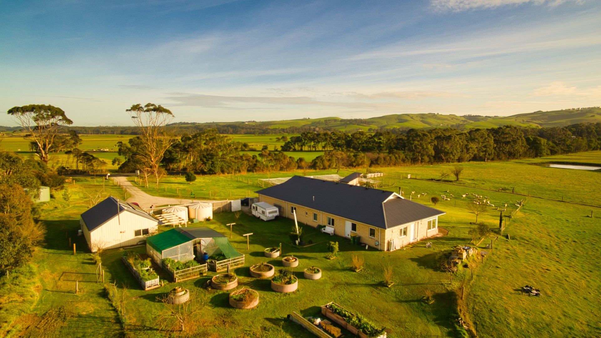 Aerial view of a rural farmhouse and outbuildings amid green fields at sunset