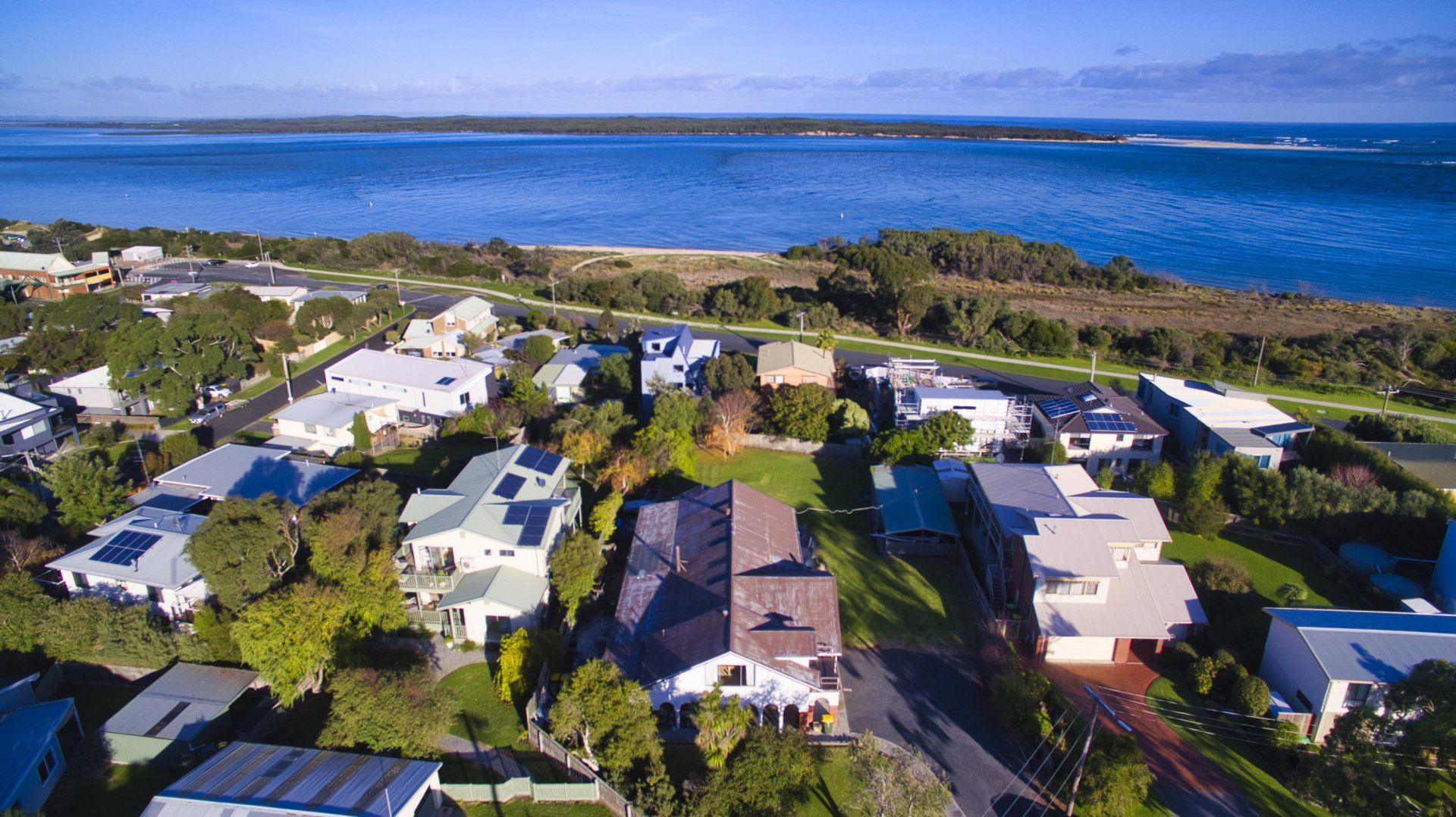 Aerial view of a coastal neighborhood with houses, trees, and blue ocean beyond