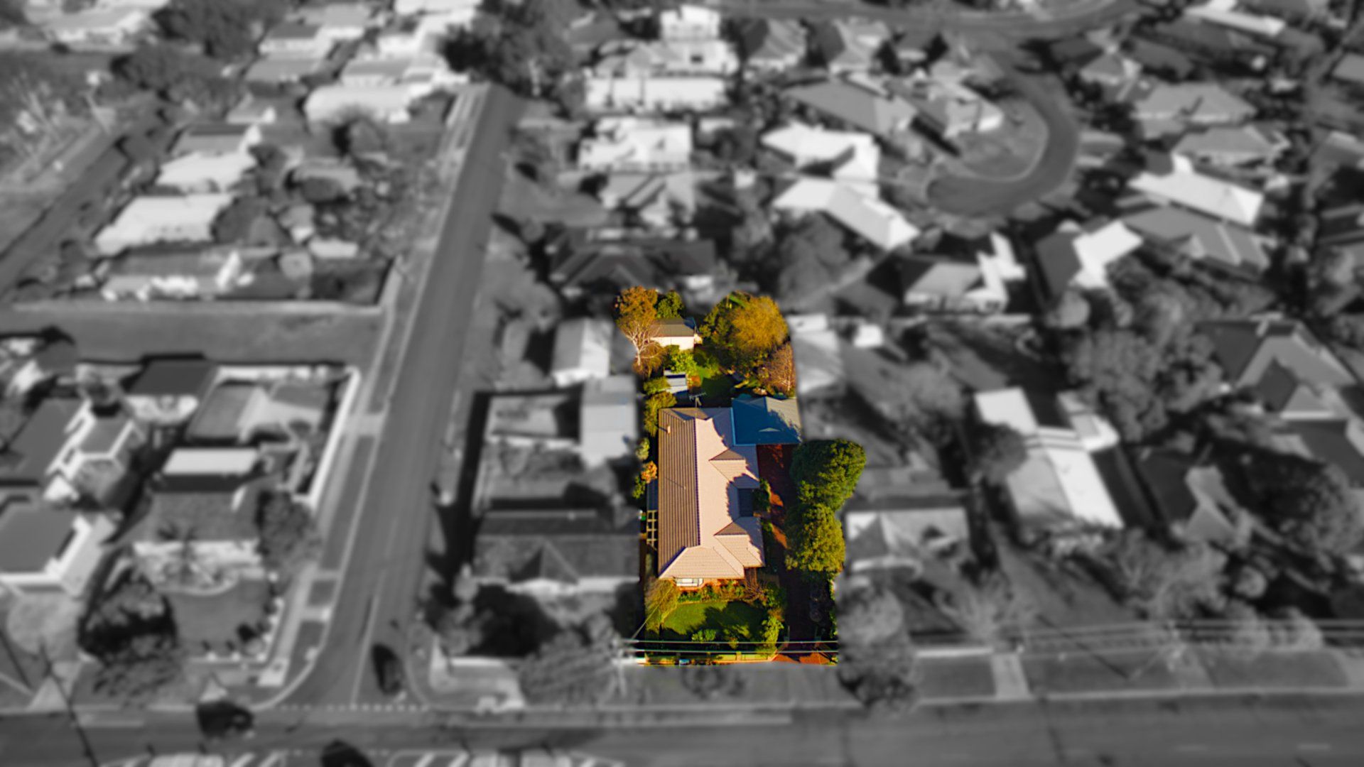 Aerial view of a house with highlighted roof amid a grayscale suburban neighborhood.