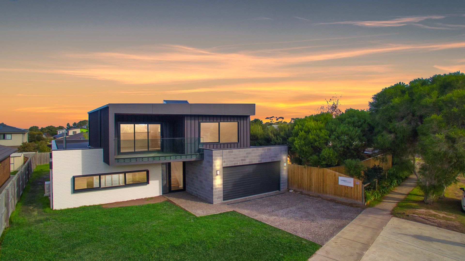 Modern two-story house with dark and white exterior at sunset, beside a grassy yard and driveway