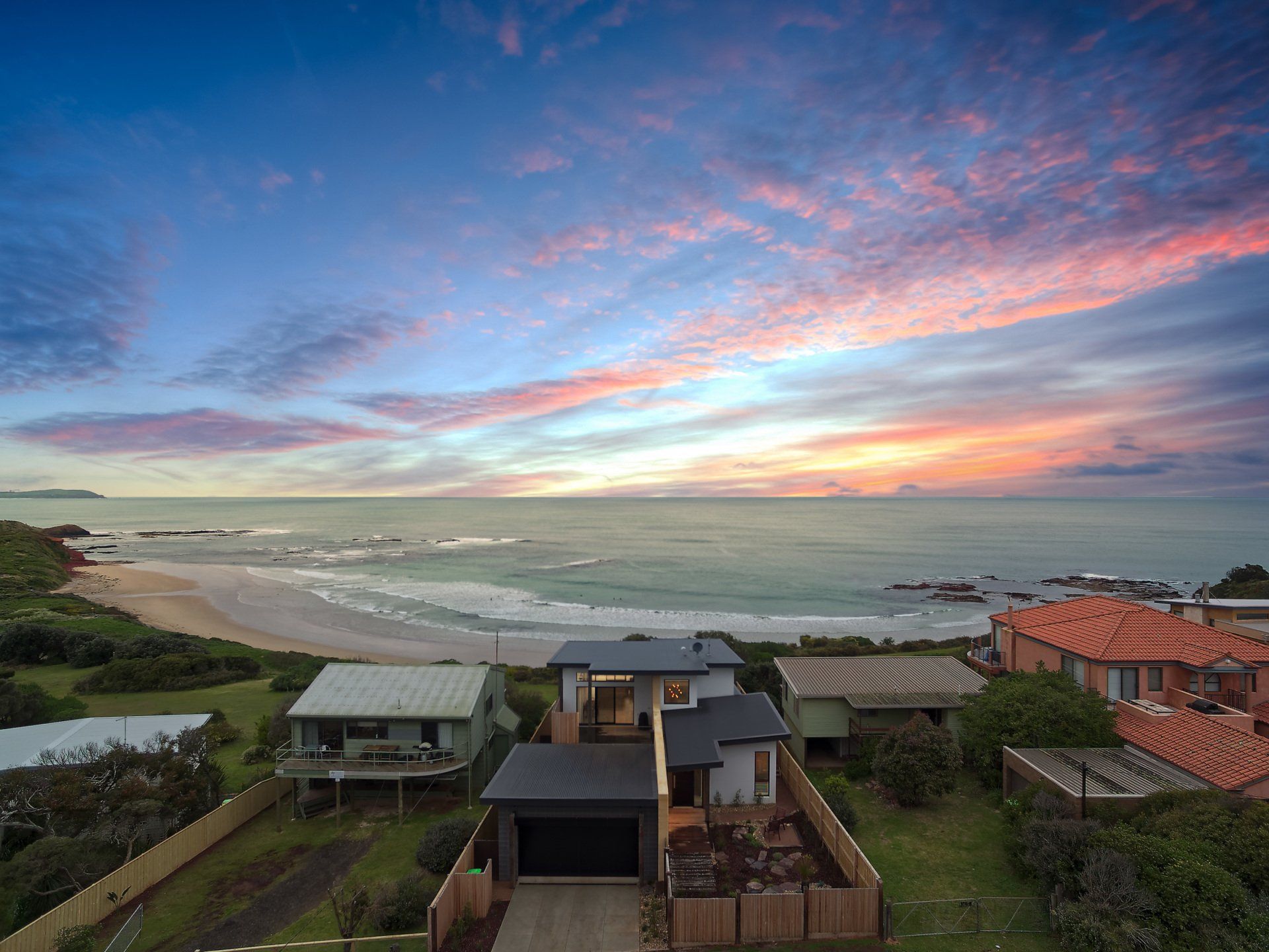 Coastal homes overlooking a calm sea at sunset with pink and blue clouds