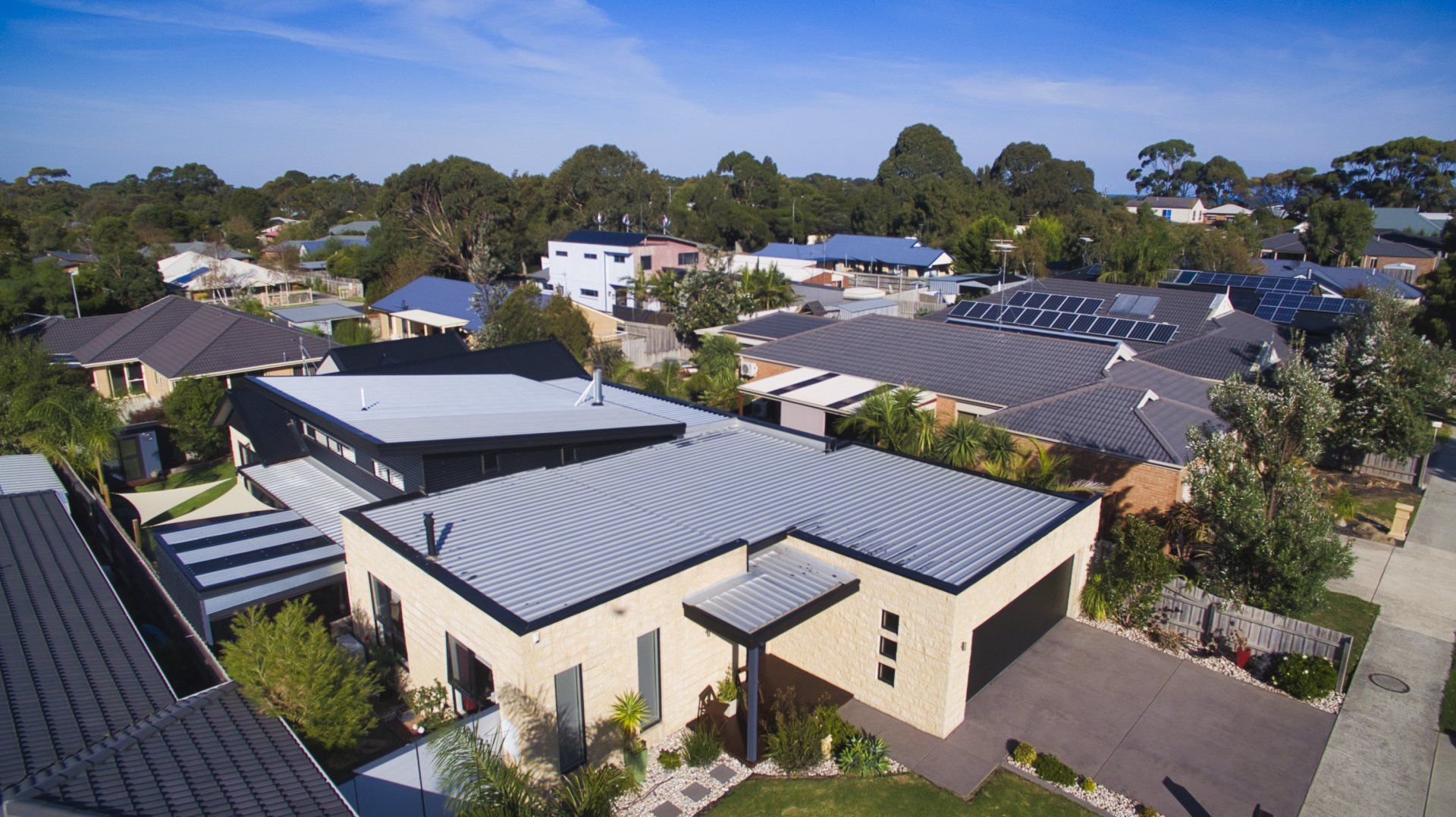 Aerial view of a suburban neighborhood with modern houses, gray roofs, and trees under a clear blue sky