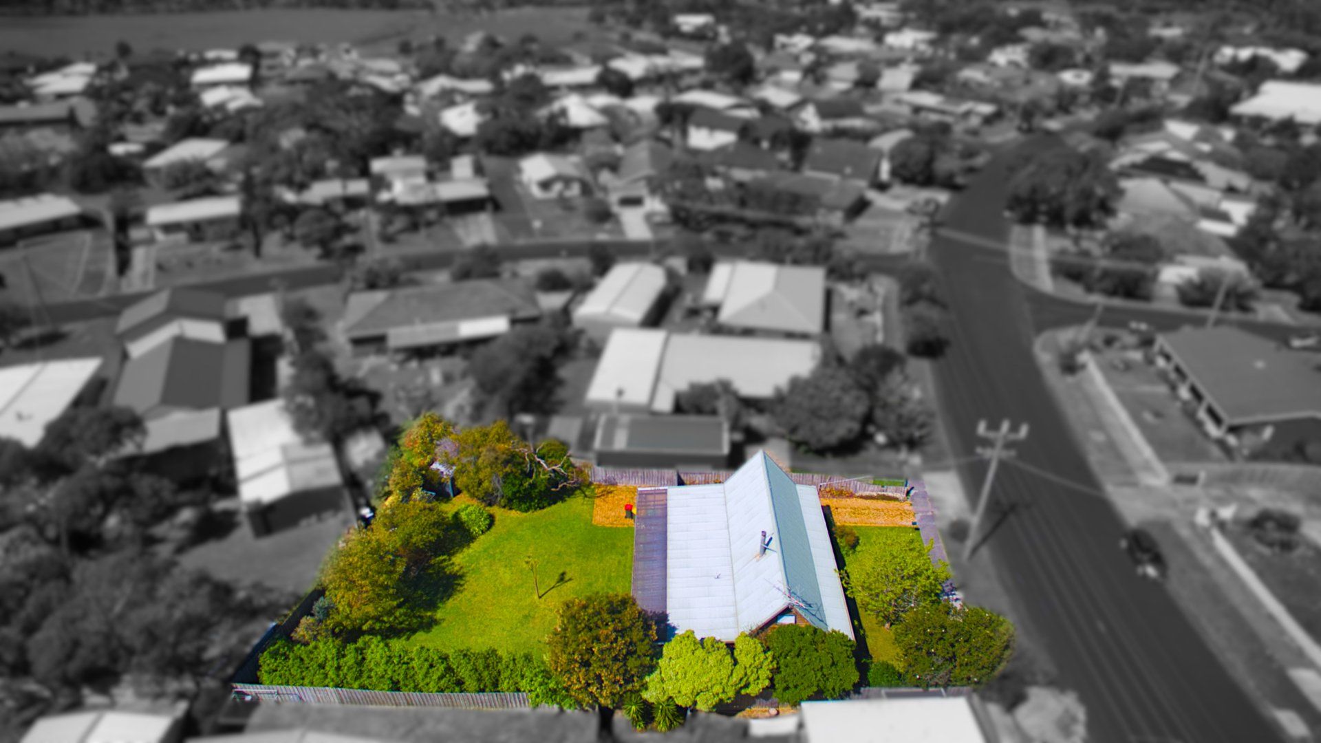 Aerial view of a house with a bright yellow-green yard amid a gray suburban neighborhood.