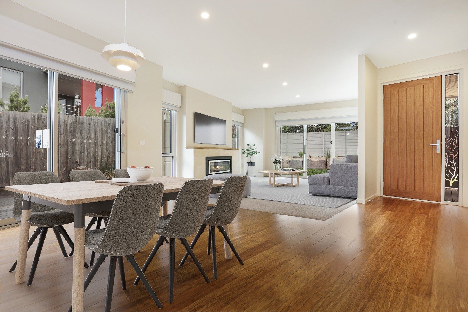 Modern open-plan dining and living area with wood floors, gray chairs, and a view to the patio