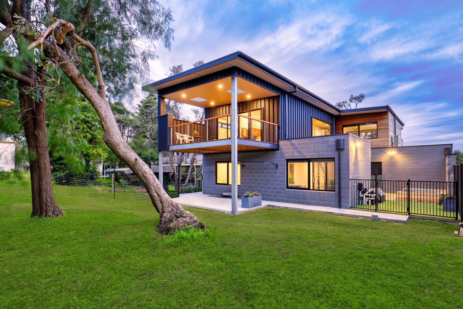 Modern two-story house with large windows and a green lawn at dusk