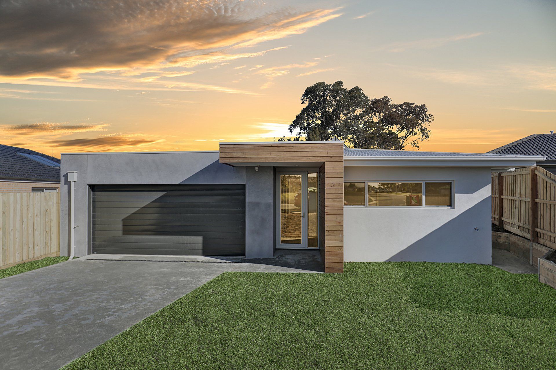 Modern single-story house exterior with garage, driveway, and front lawn at sunset