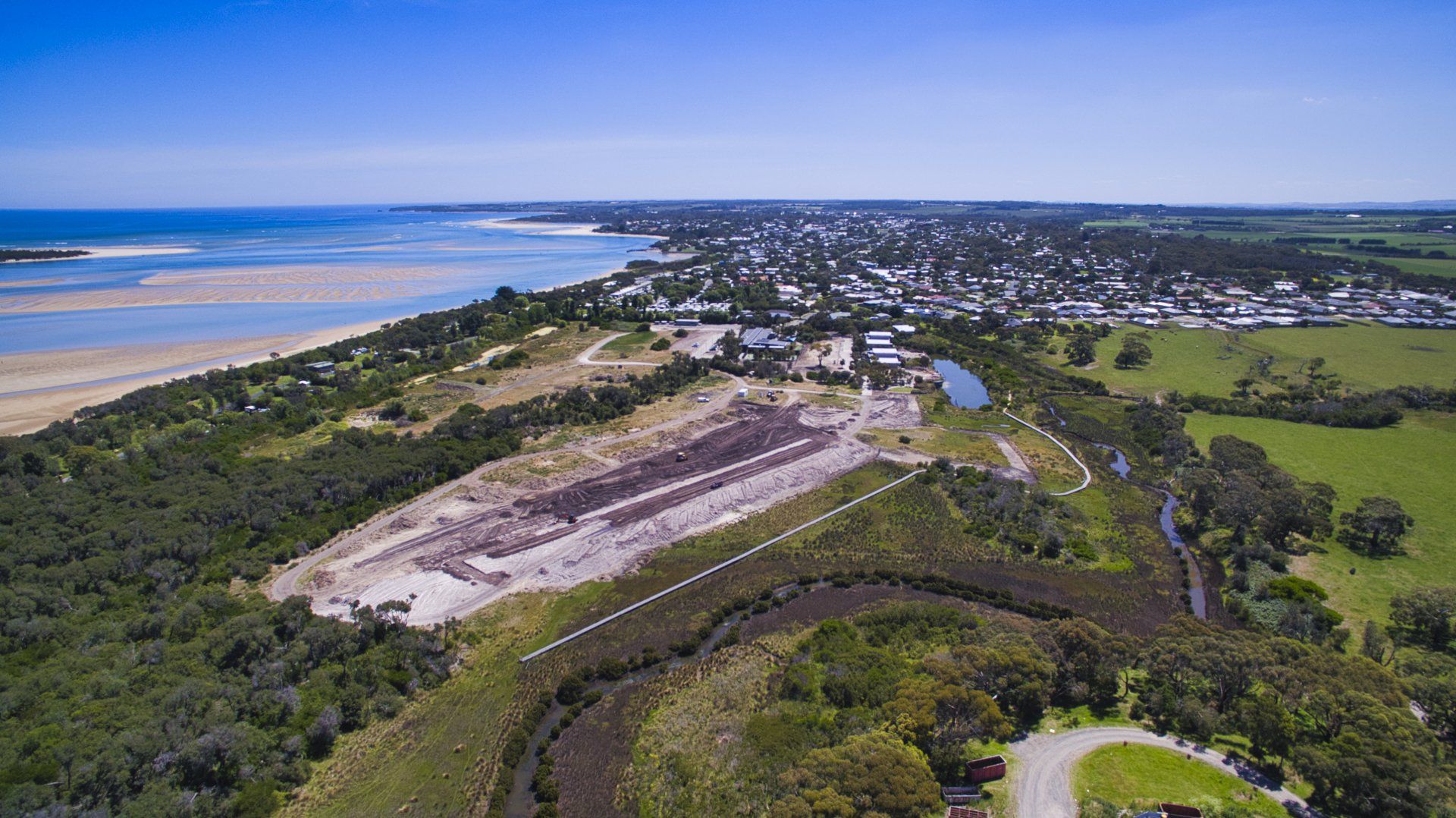 Aerial view of a coastal town, beach, green fields, and a river under a blue sky