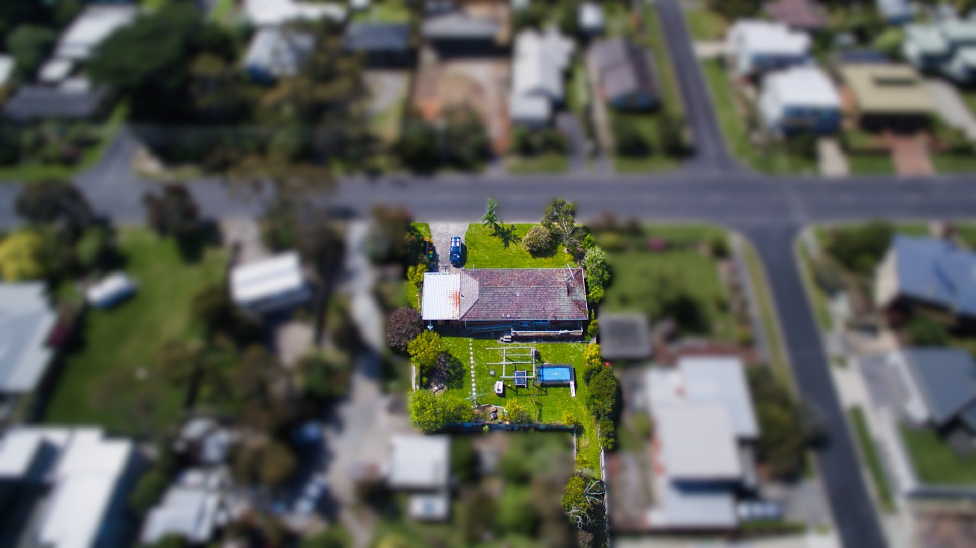 Aerial view of a house highlighted in yellow, surrounded by a blurred suburban neighborhood.