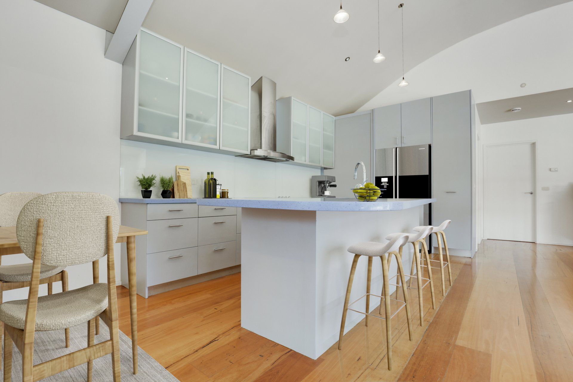 Modern white kitchen with island, bar stools, glass cabinets, and light wood floors