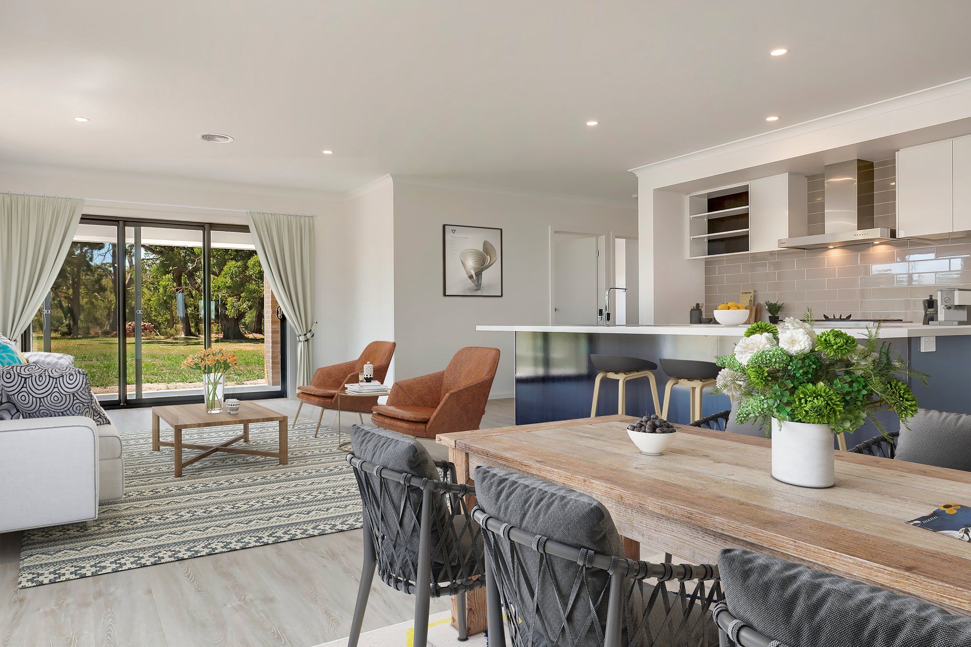 Bright modern open-plan living room and kitchen with sliding glass doors, tan chairs, and a wooden island countertop