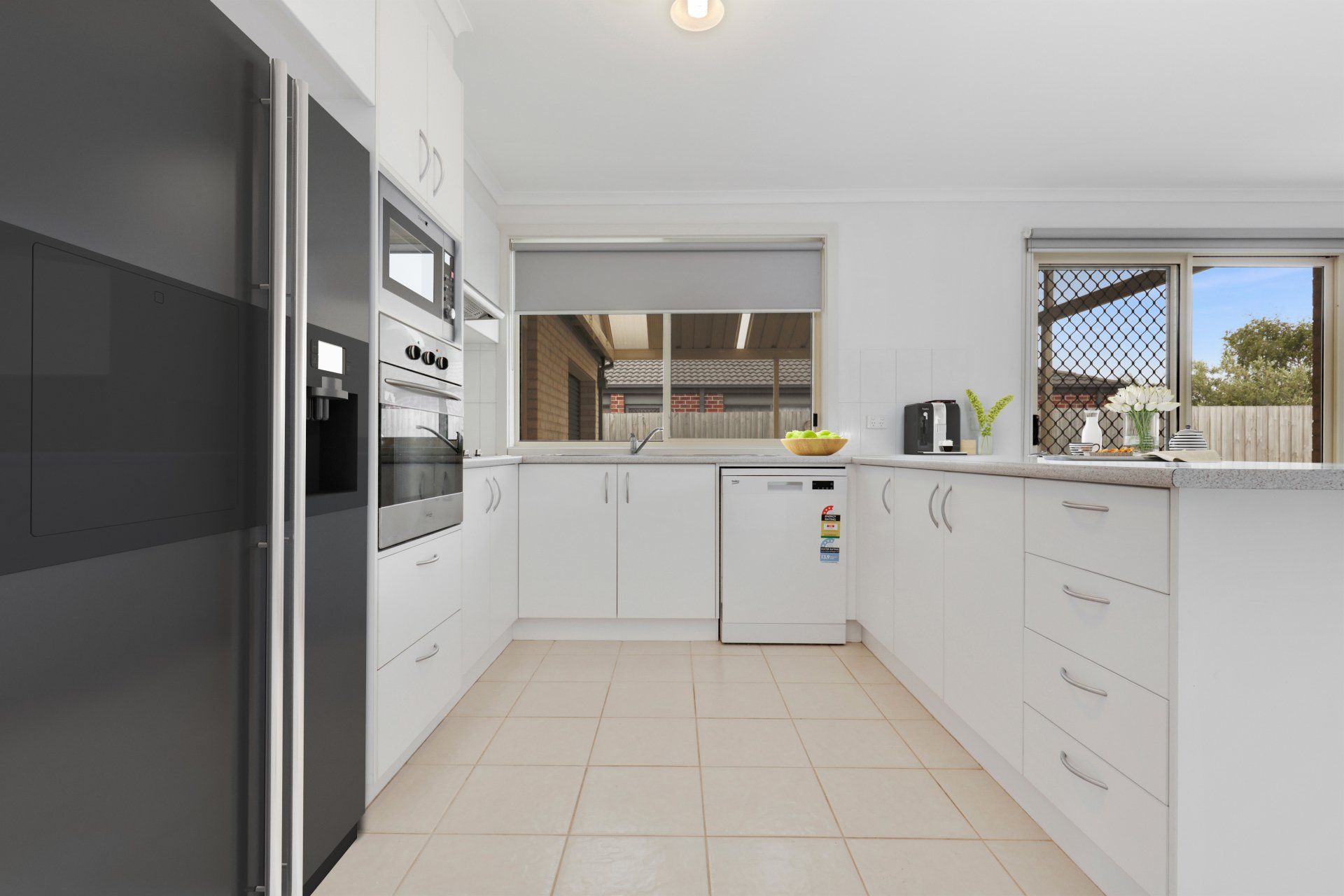 Modern white kitchen with tiled floor, built-in ovens, and a window over the sink