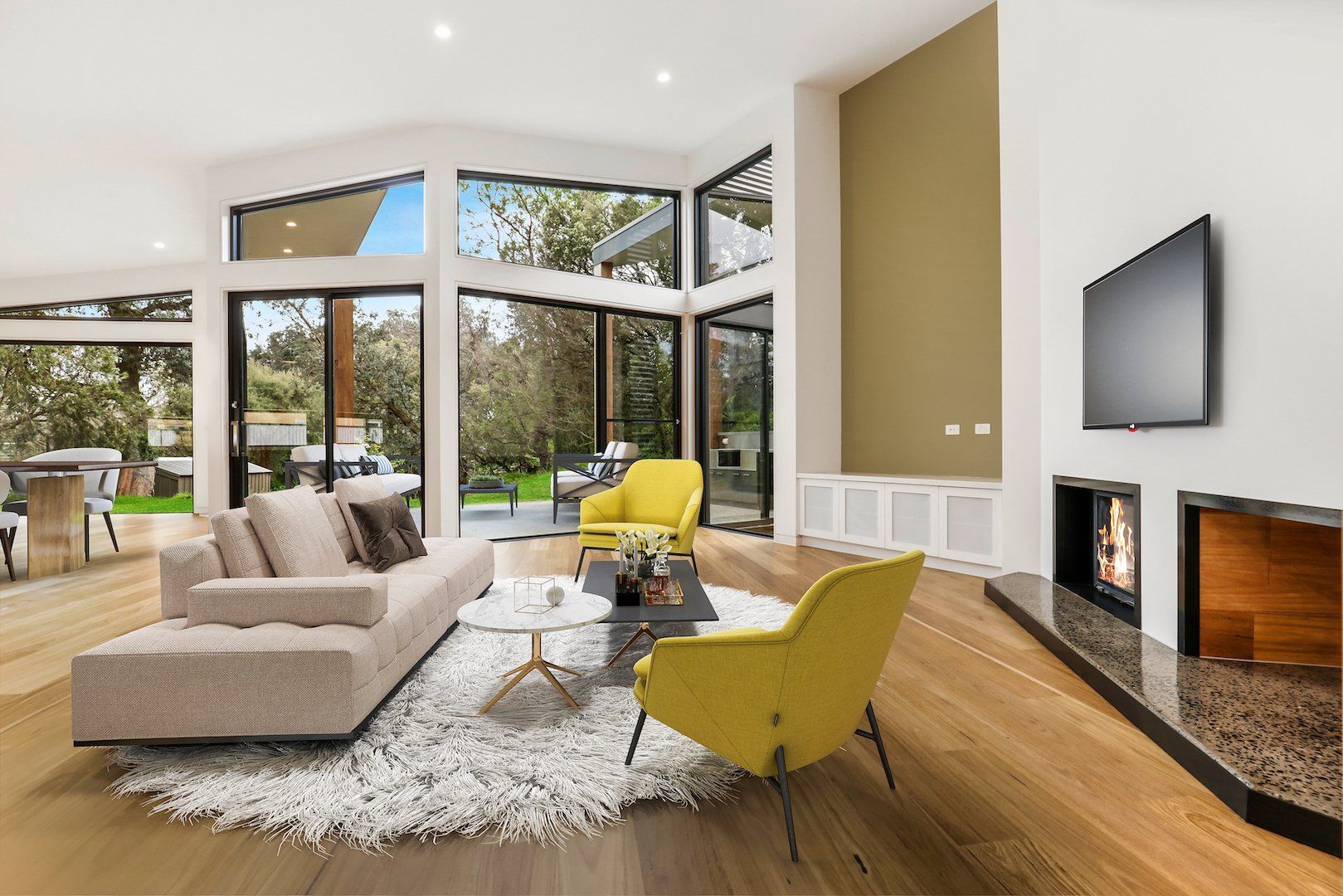 Modern living room with beige sofa, yellow chairs, large windows, and a fireplace