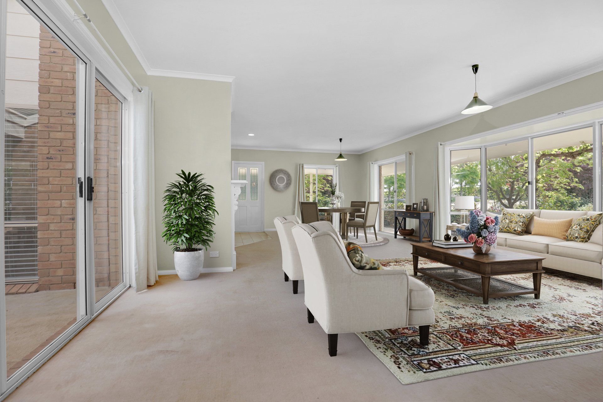Bright living room with beige chairs, sofa, coffee table, large windows, and sliding glass door