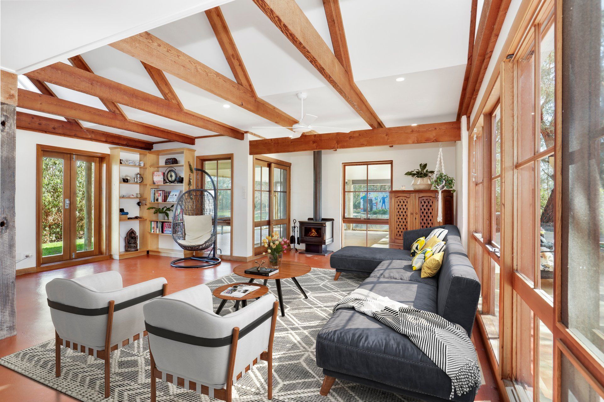 Bright sunroom with wood beams, large windows, and black-and-white seating around a fireplace.
