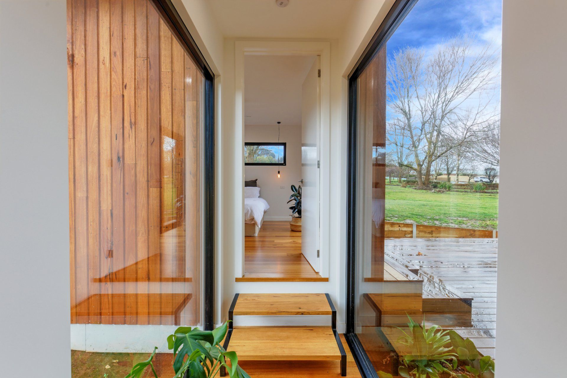 Front entry with wood siding, glass doors, and a view through to a bright interior and garden beyond