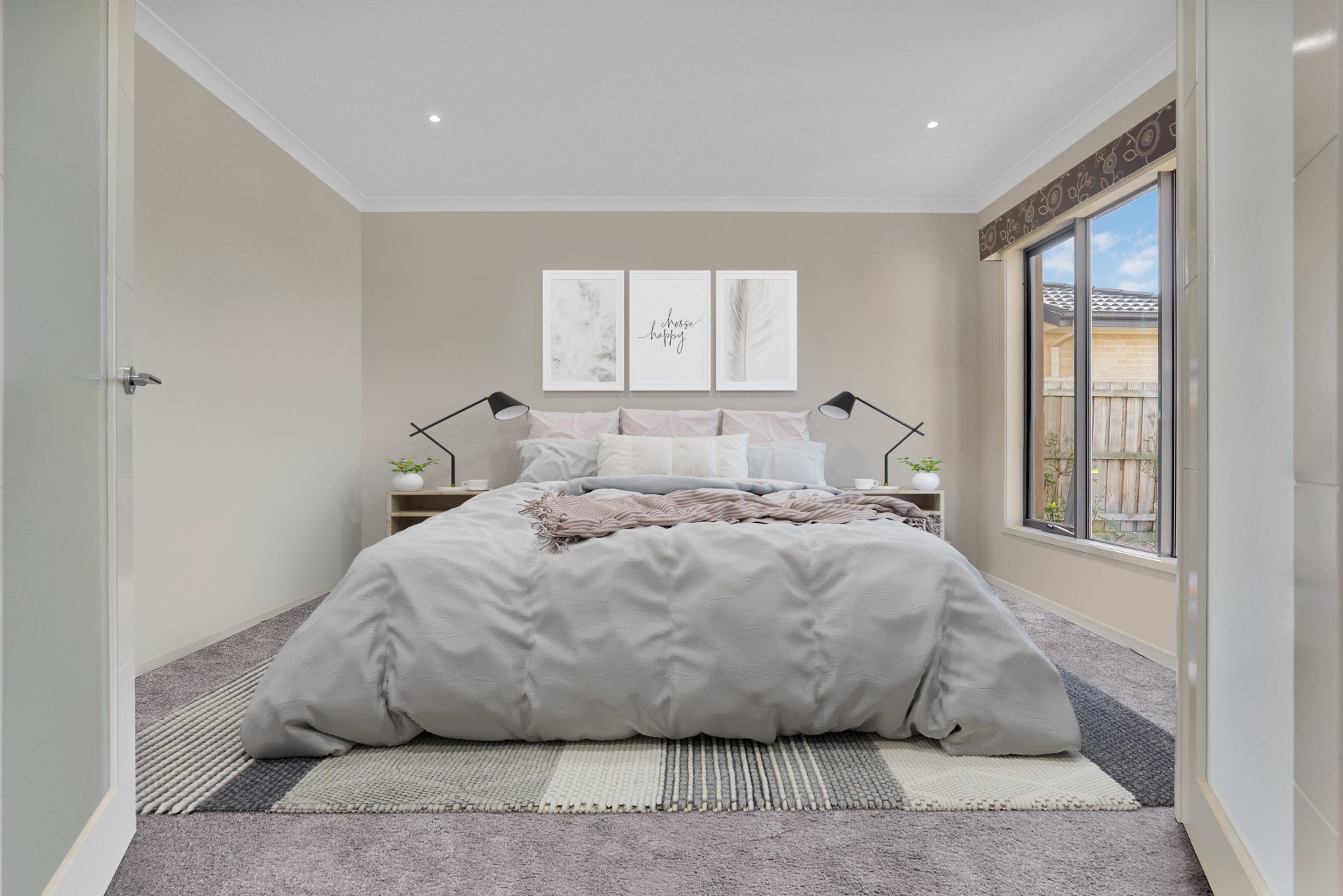 Bright bedroom with a neatly made bed, gray walls, bedside lamps, and a large window overlooking trees.
