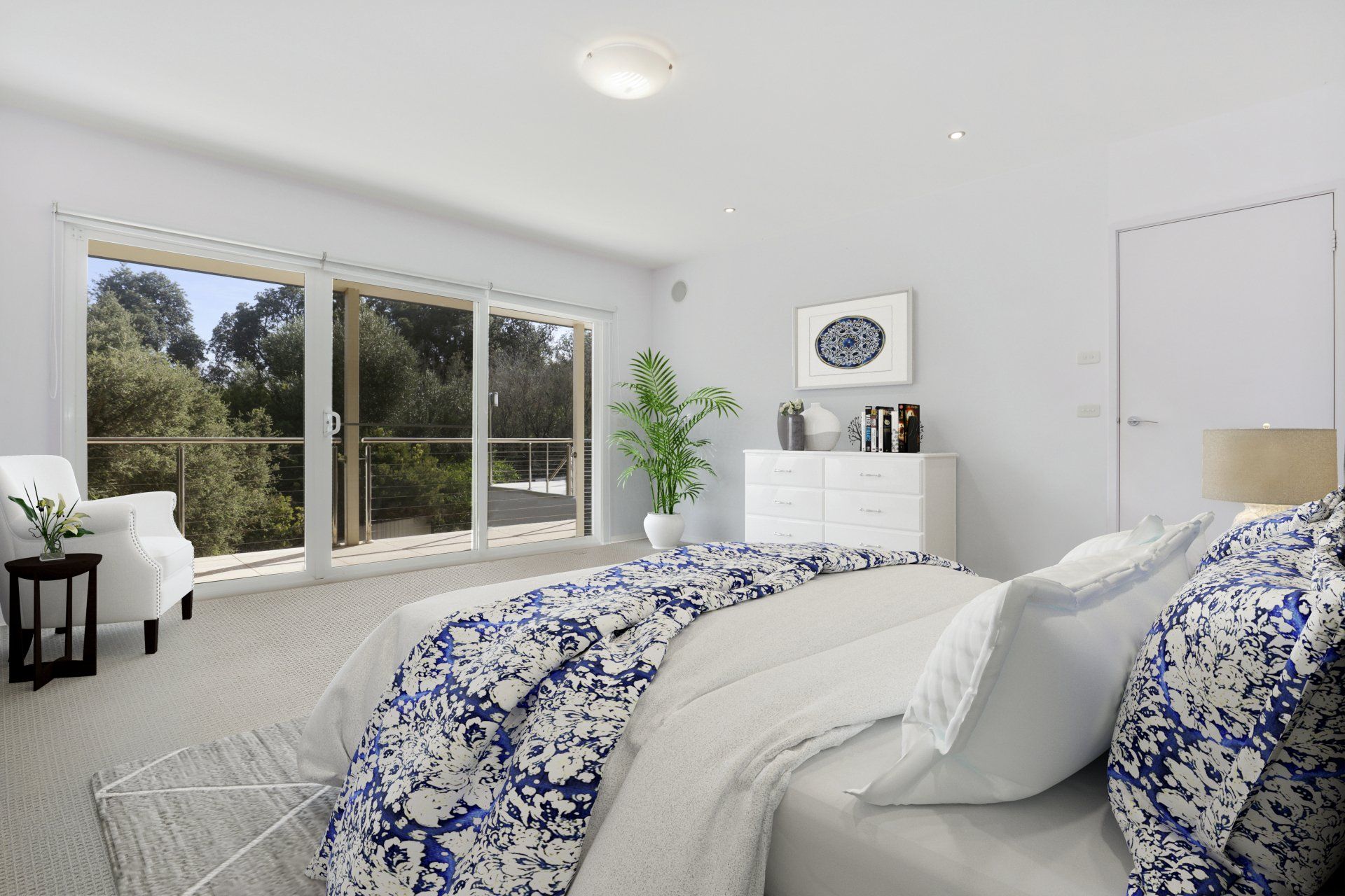 Bright white bedroom with blue floral bedding, large windows, and a potted plant.
