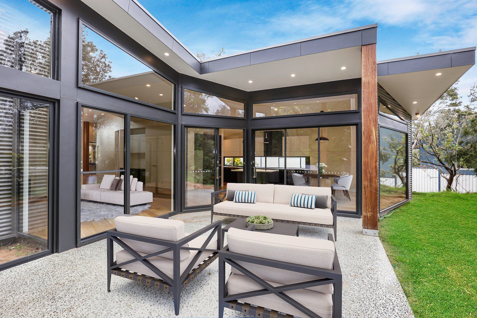 Modern patio with outdoor sofa, chairs, and gravel beside large glass doors and a covered roof.