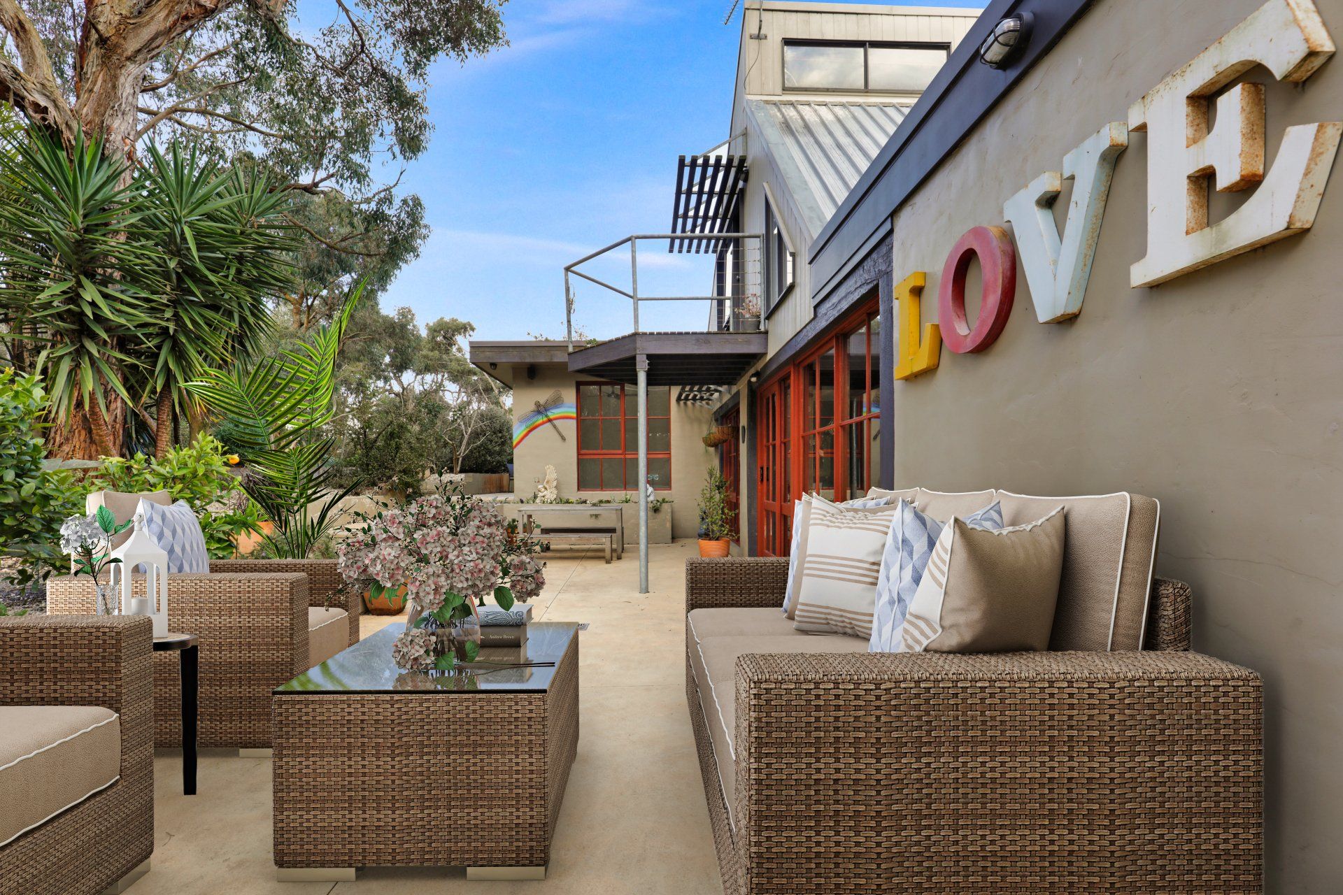 Outdoor patio with wicker seating, potted plants, and large wall letters reading “LOVE”