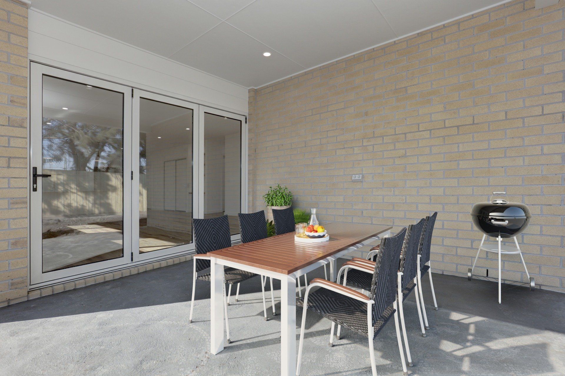 Covered patio with outdoor dining table, chairs, and a charcoal grill by glass doors