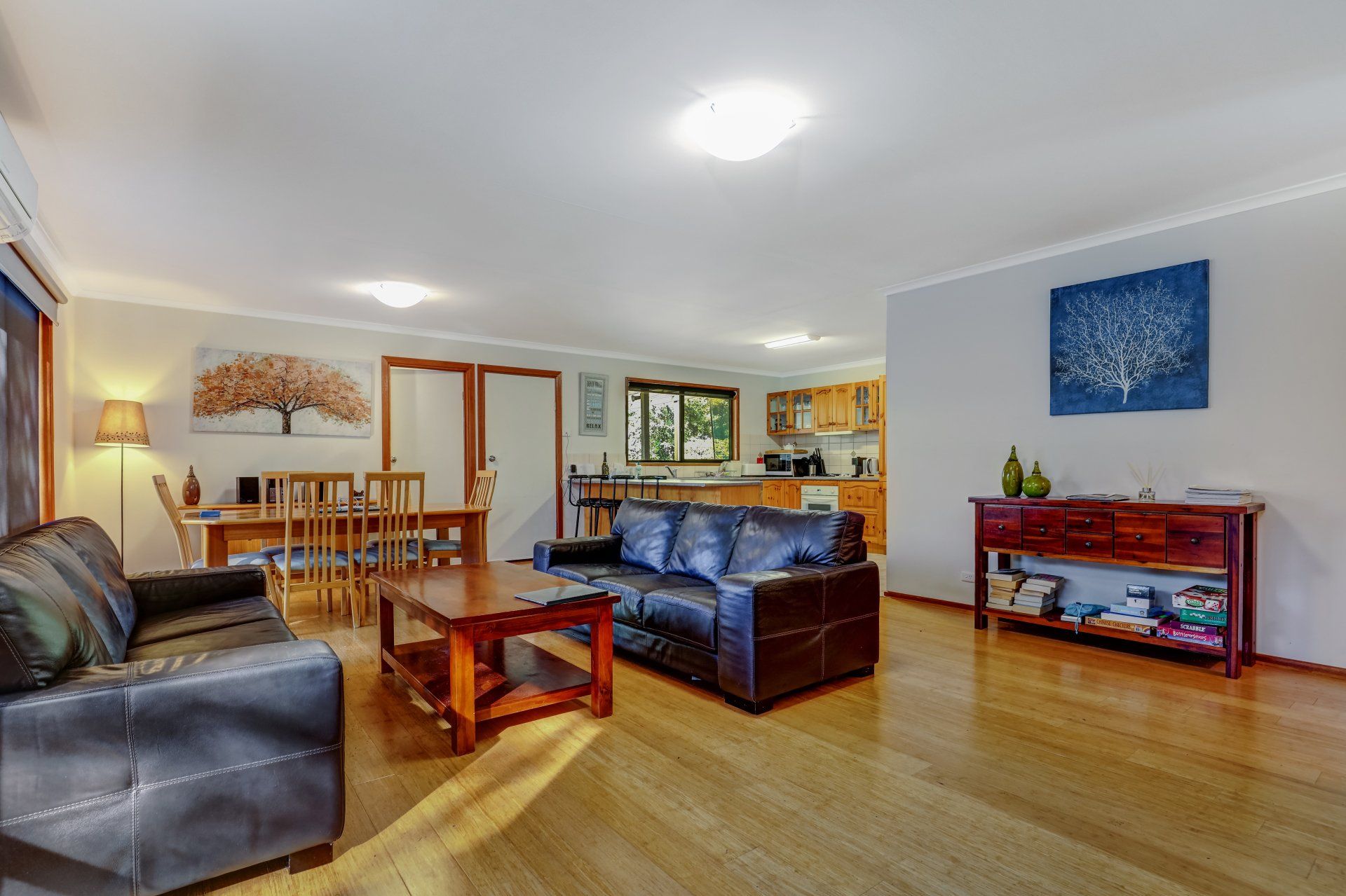 Bright living room with leather sofas, wooden coffee table, dining area, and blue wall art