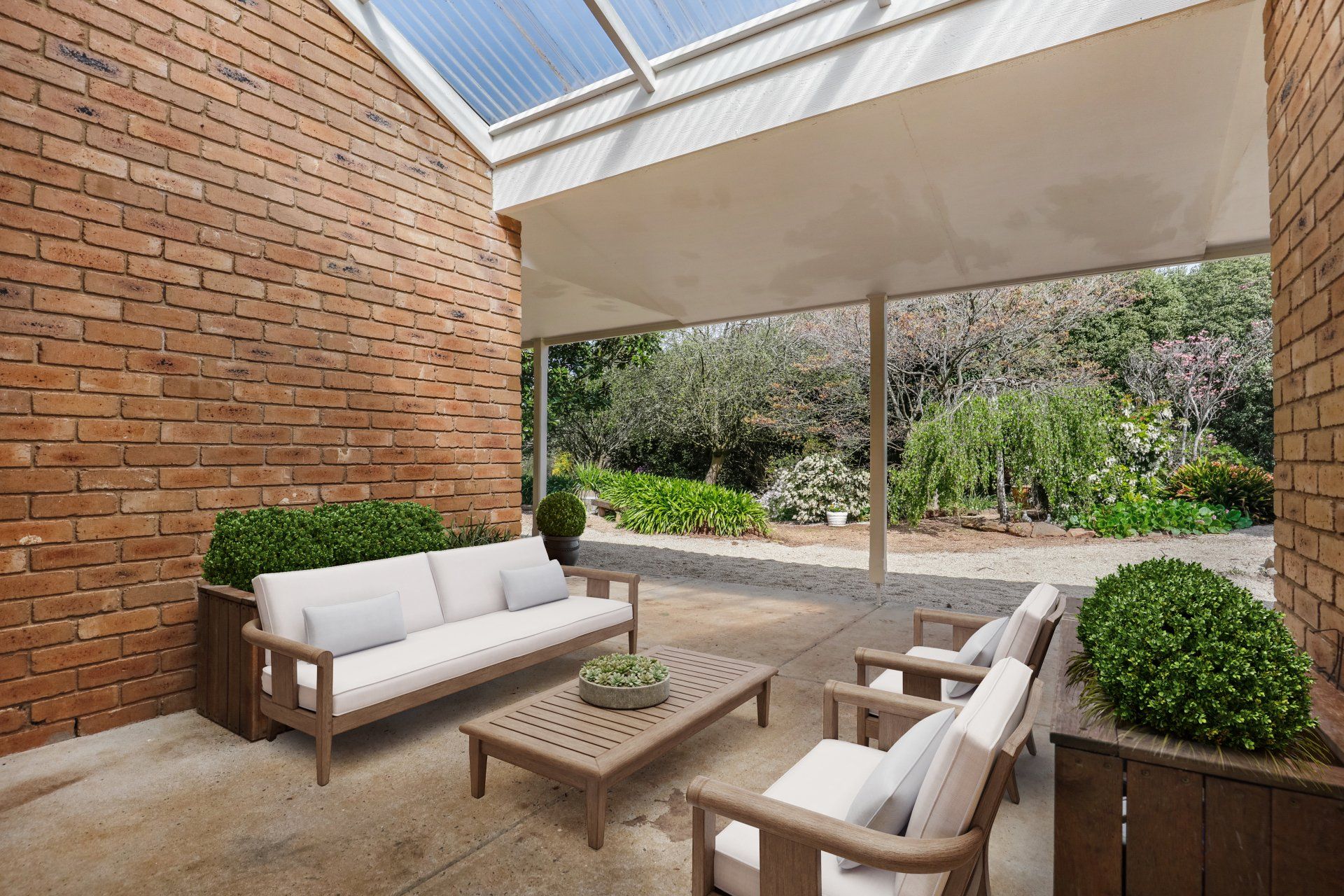 Outdoor patio with white cushioned seating, wooden coffee table, brick wall, and garden view