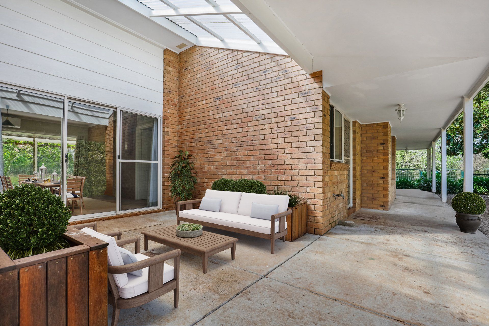 Covered brick patio with modern seating, concrete floor, and large windows beside a home