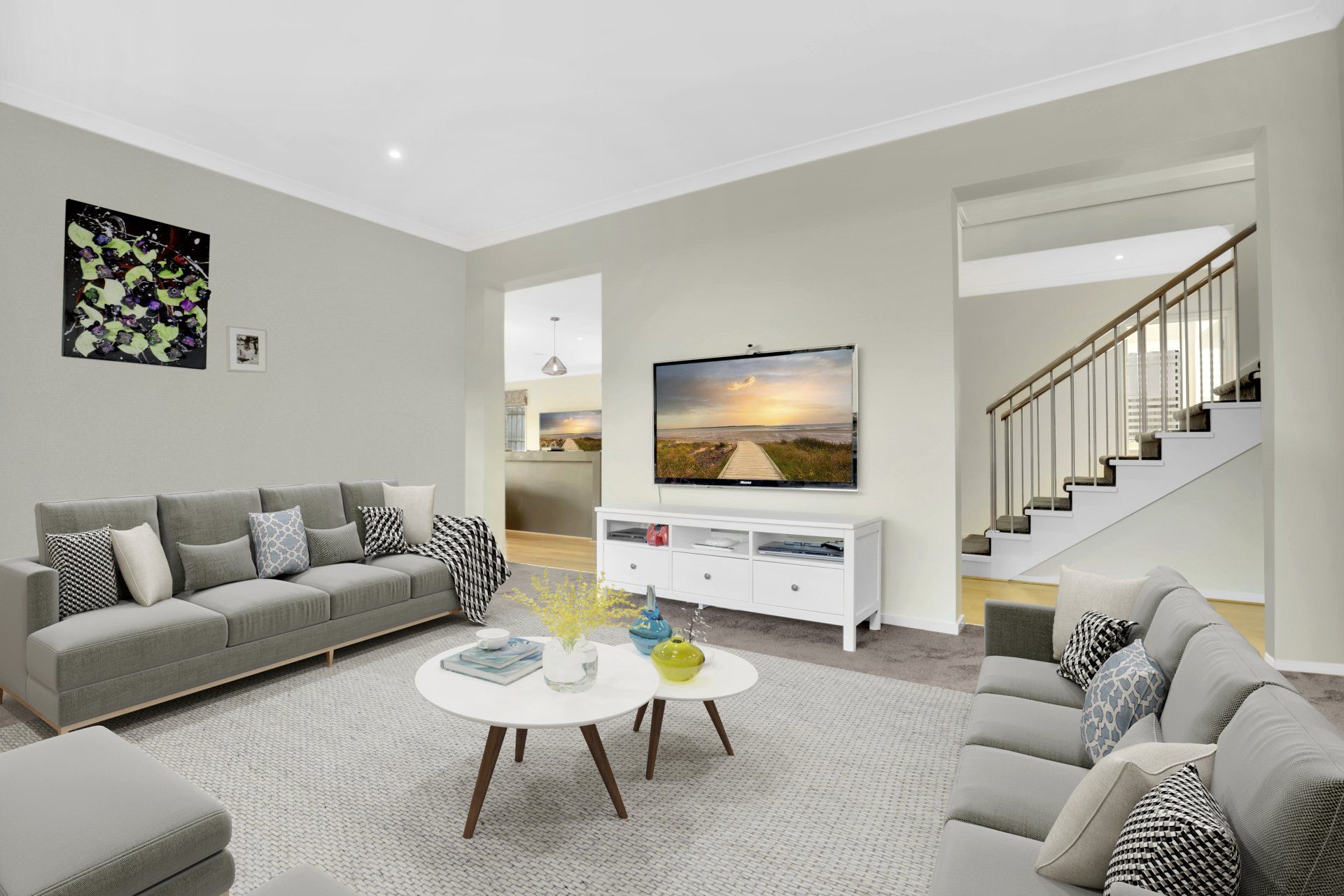 Bright living room with gray sofas, white console, staircase, and wall art on light gray walls.