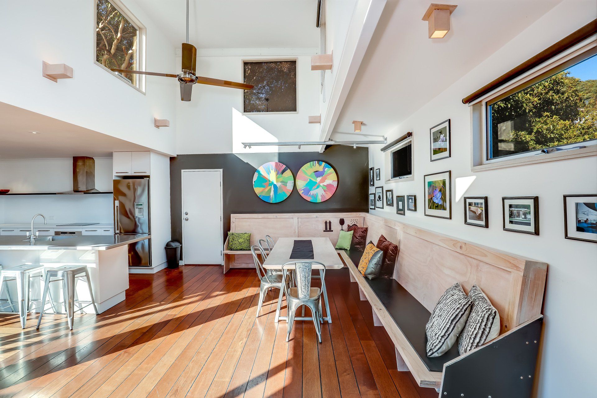 Bright modern living room with wood floors, vaulted ceiling, large windows, and colorful wall art