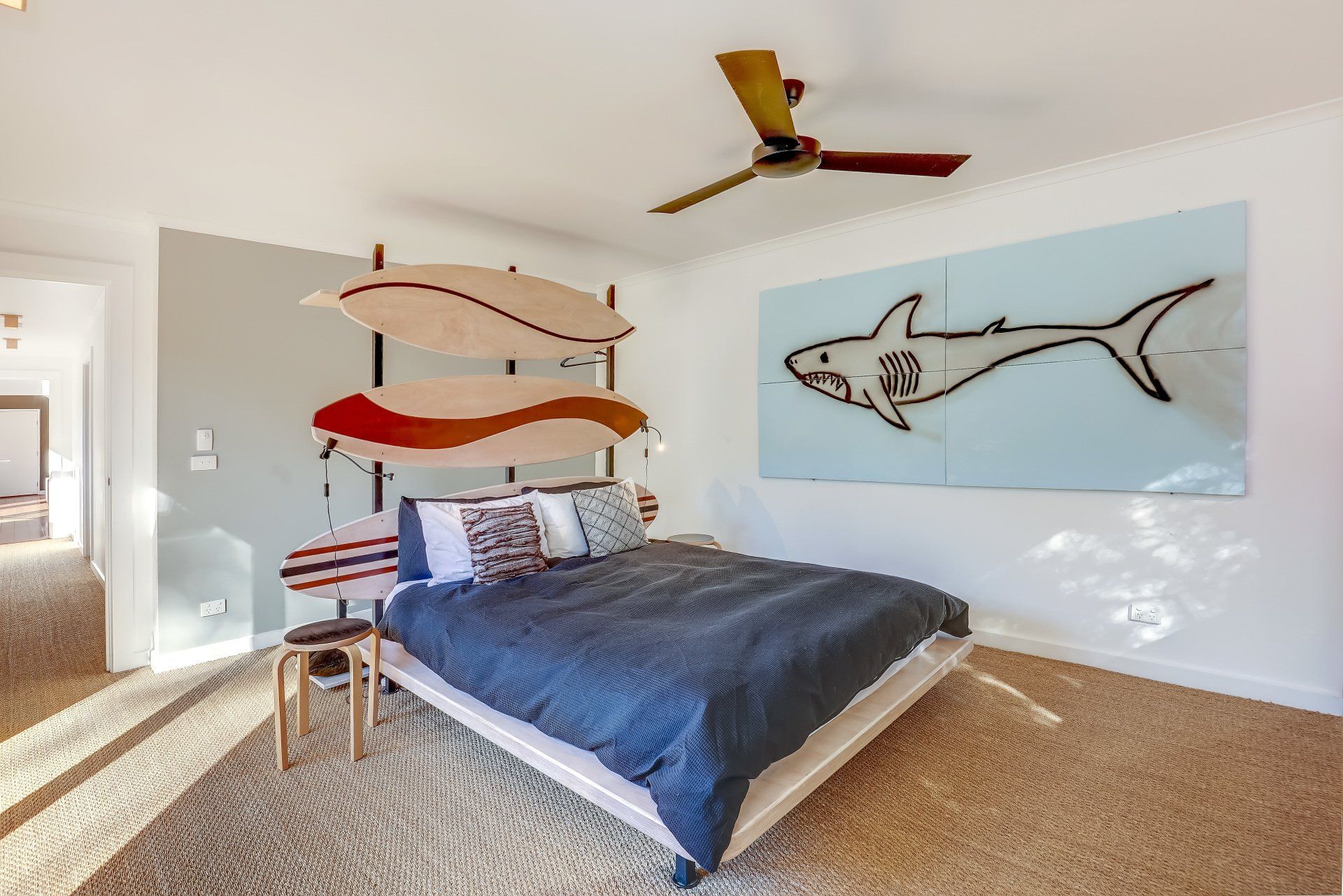 Bright bedroom with a bed, surfboard wall art, and a shark mural on a light blue wall.