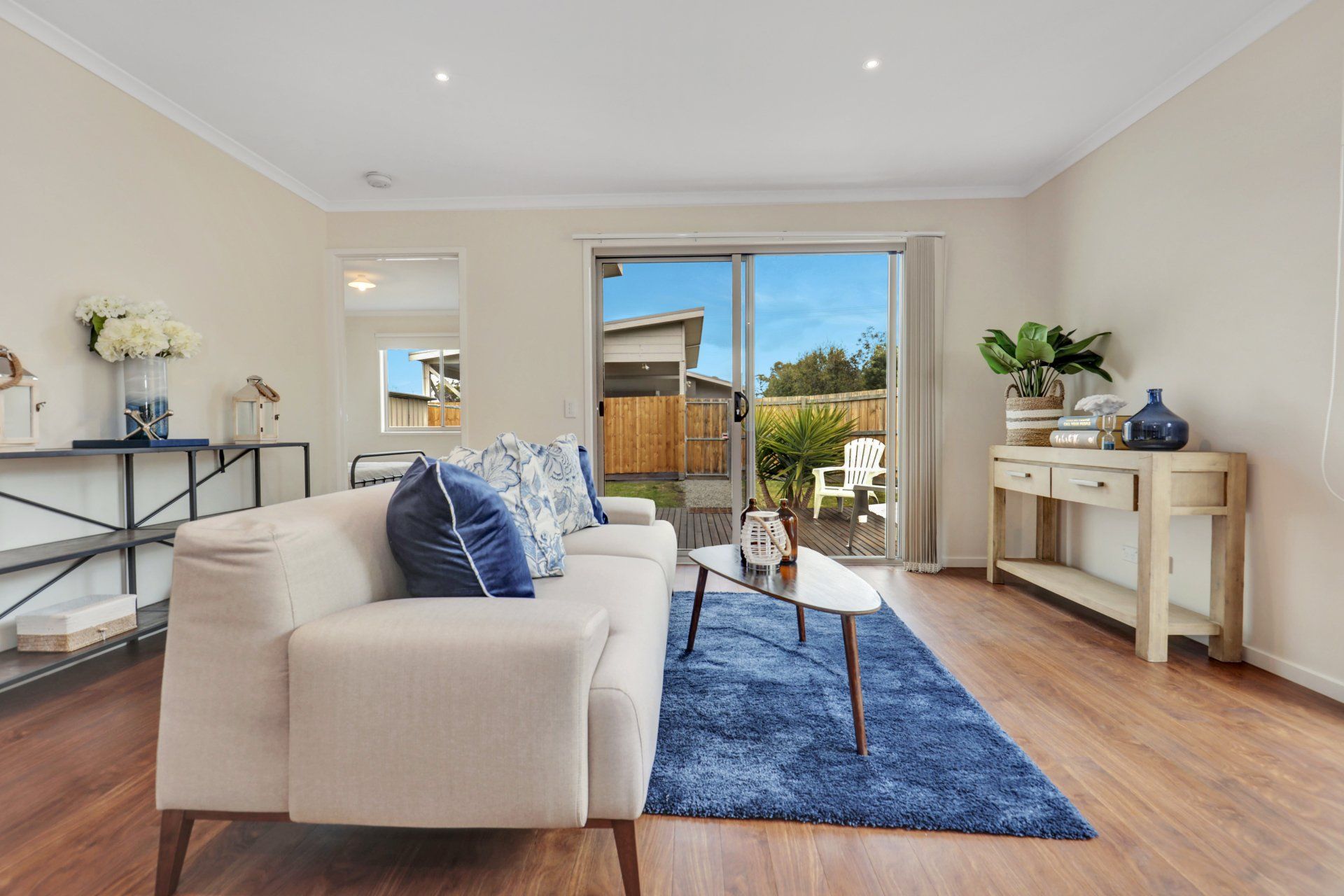 Bright living room with beige sofa, blue rug, console table, and sliding doors to a sunny patio.