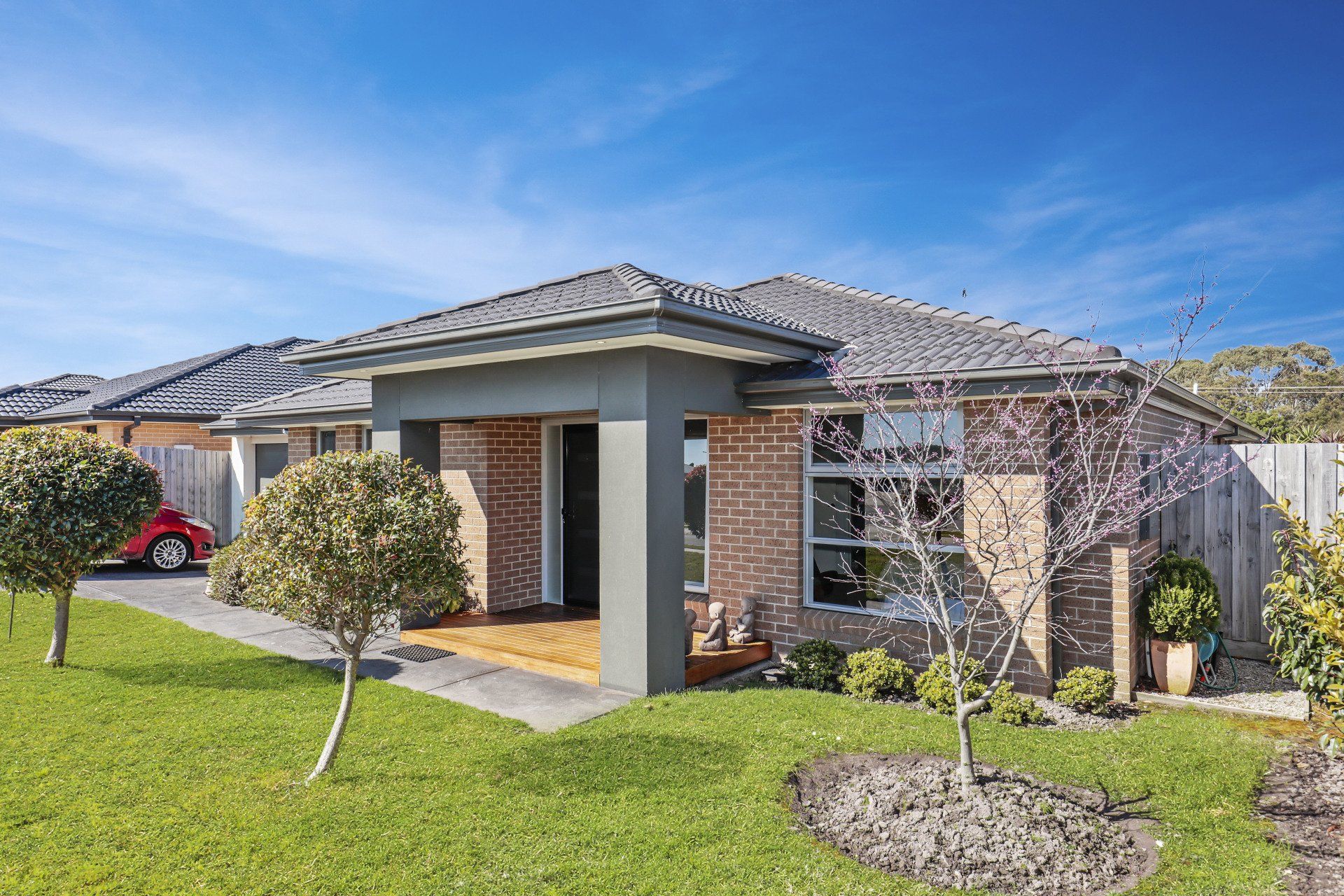 Modern single-story brick house with a tiled roof, front lawn, and clear blue sky