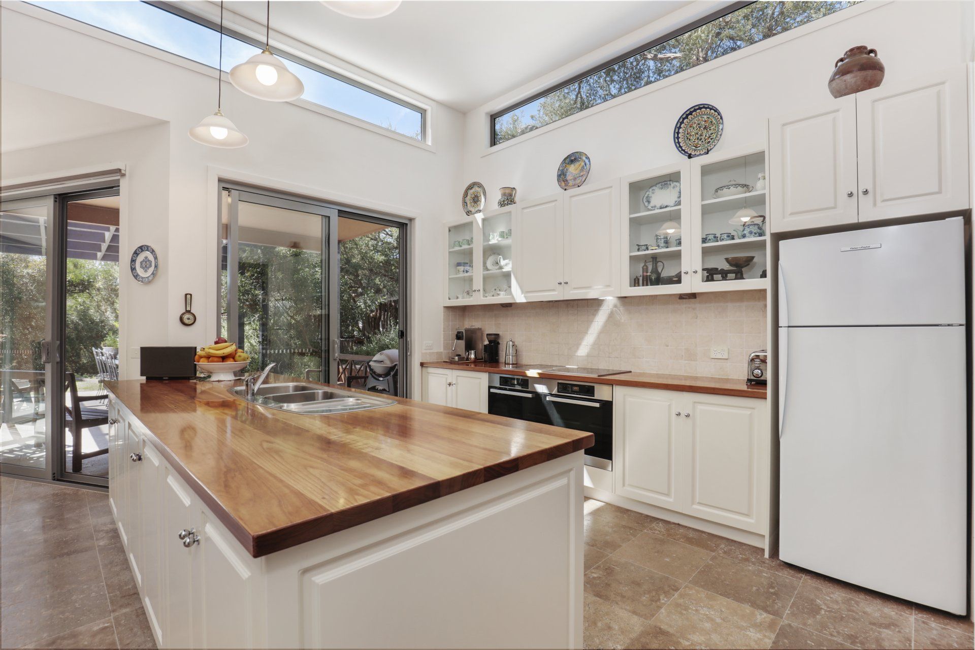 Bright kitchen with white cabinets, a wooden island, and a large window overlooking greenery