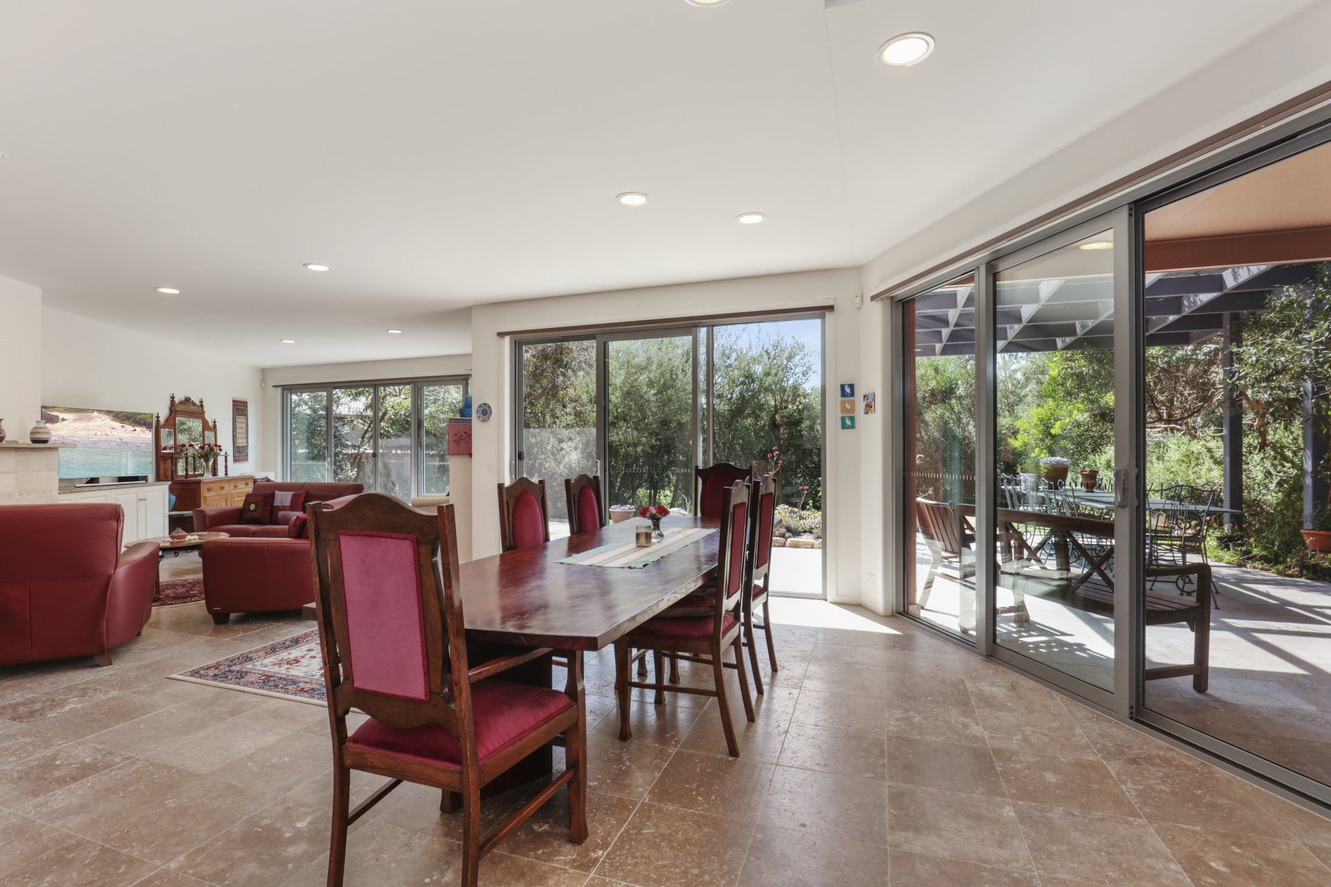 Bright dining and living room with red chairs, wood table, and large sliding glass doors to a patio.