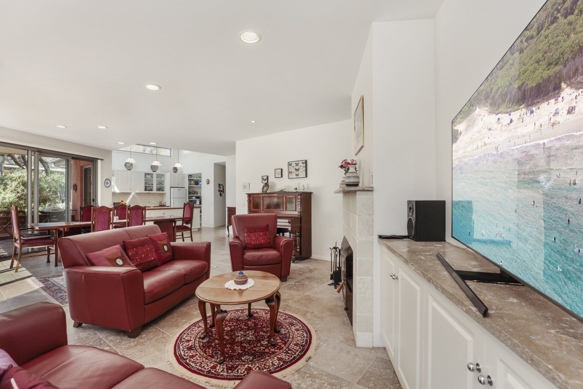 Bright living room with red leather sofas, glass coffee table, and a large ocean mural on the wall.