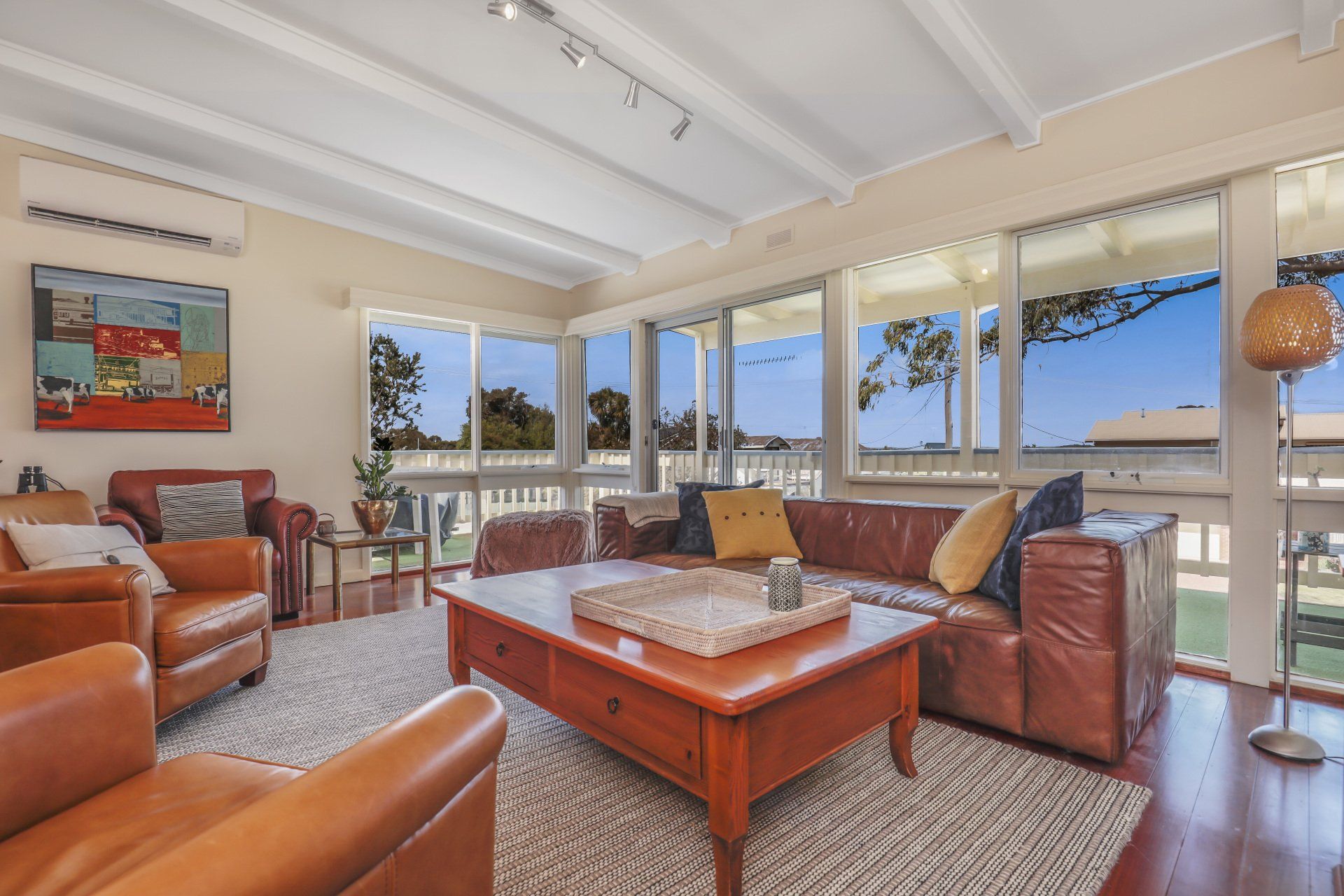 Bright living room with leather sofas, a coffee table, and large windows overlooking a coastal view