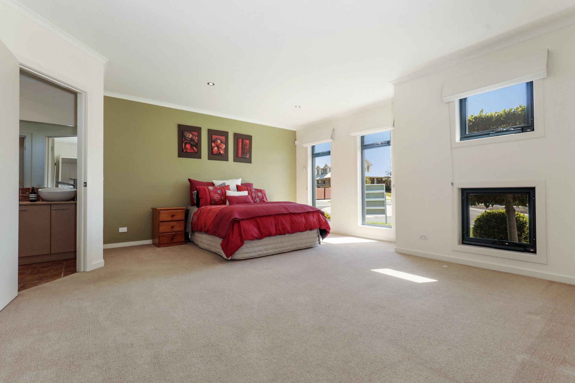 Spacious bedroom with a red bedspread, beige carpet, fireplace, and open doorway to a balcony.