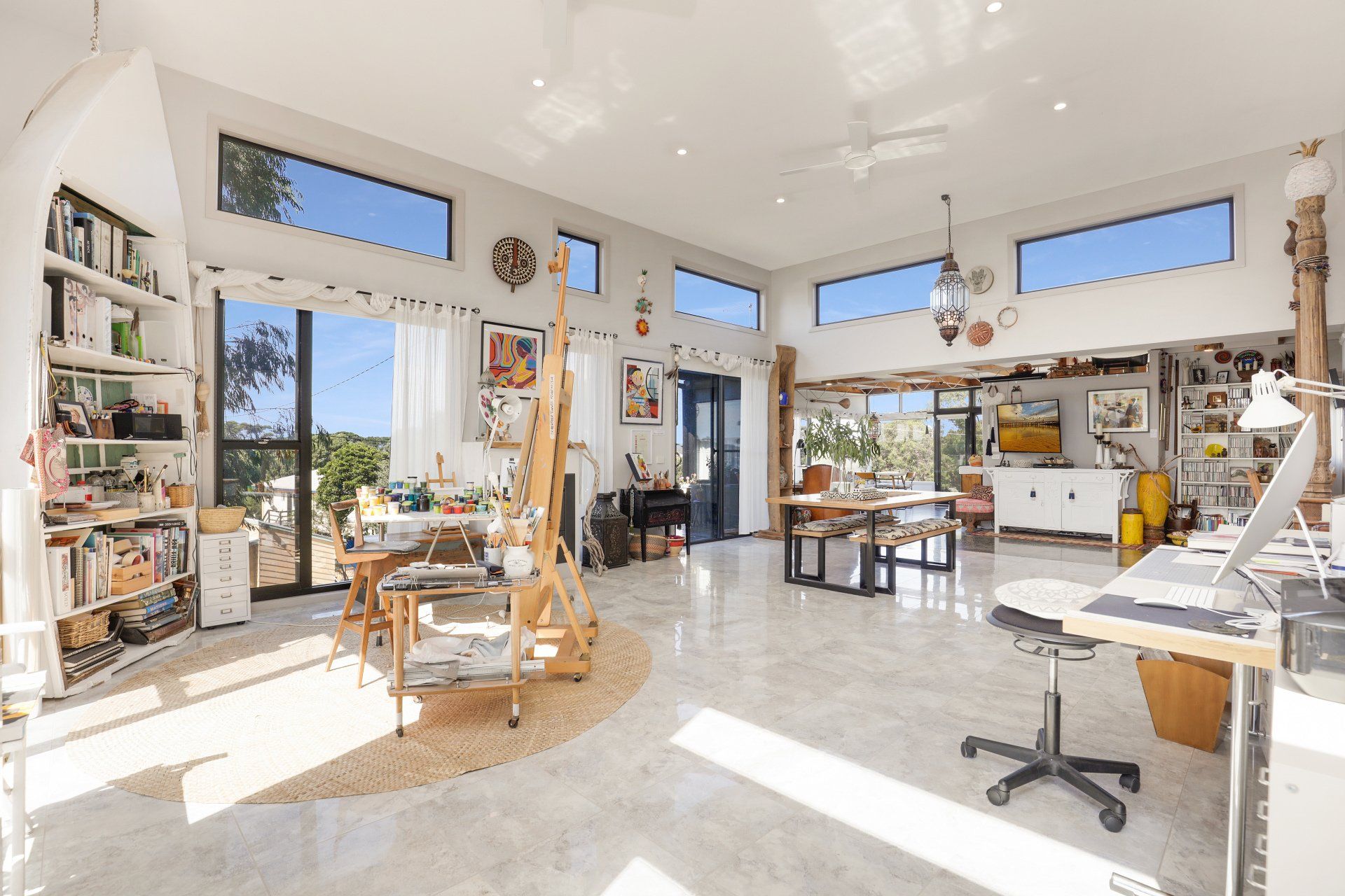Bright art studio with large windows, shelves, easels, tables, and a sunlit tiled floor