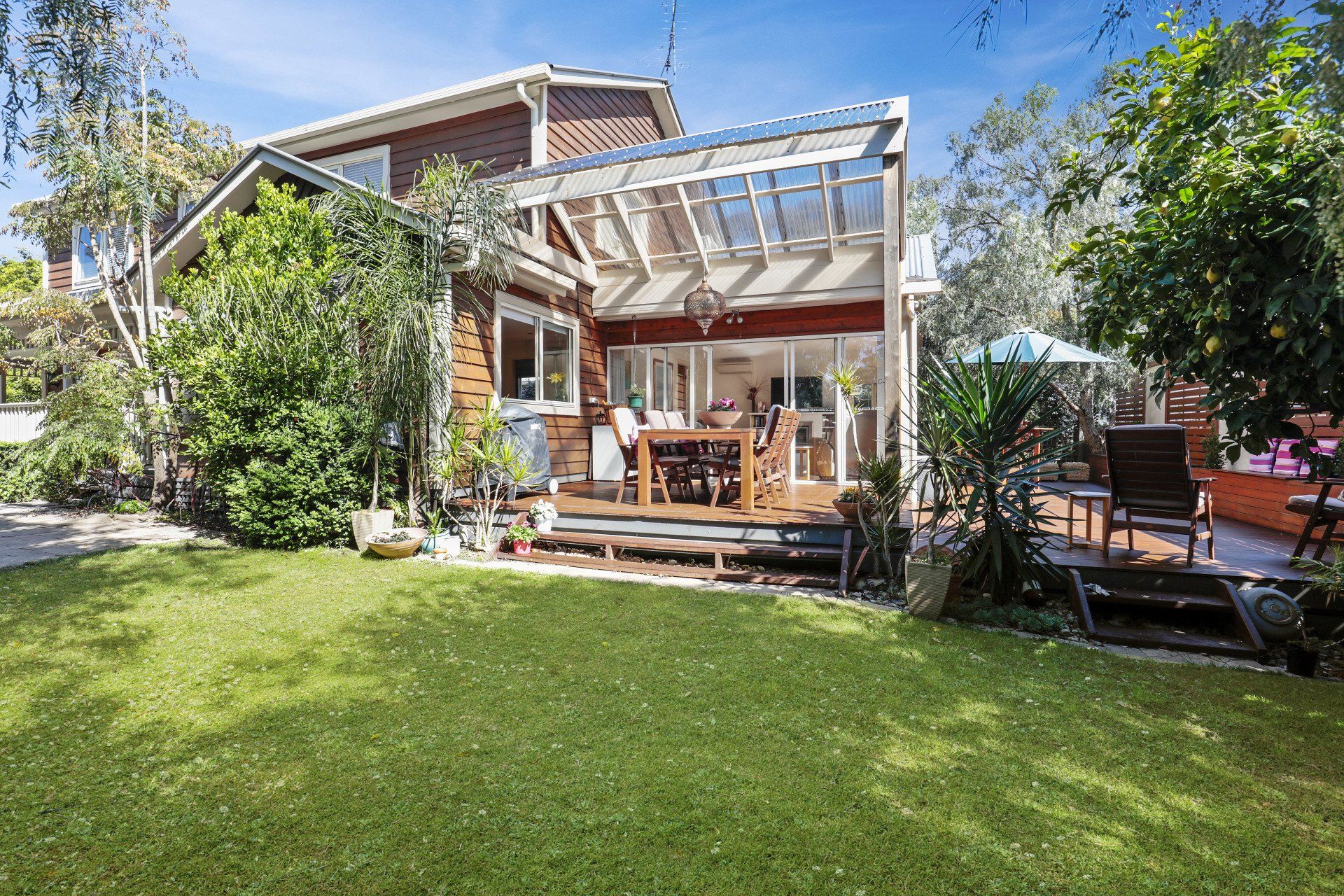 Backyard patio with wooden deck, pergola, outdoor seating, and lush green lawn beside a house