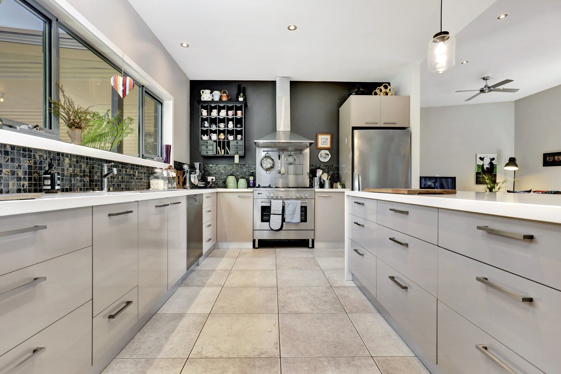 Modern white kitchen with island, stainless appliances, tiled floor, and black backsplash.